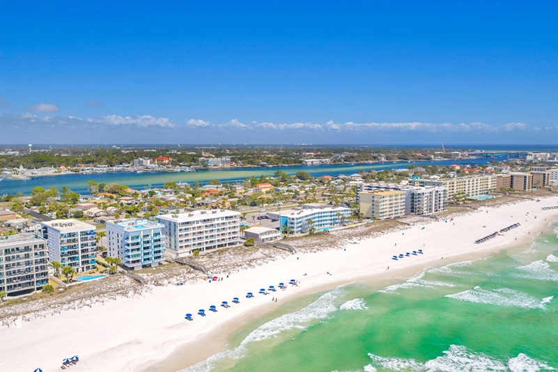 Aerial view of Fort Walton Beach, Florida, with white sand beaches, emerald-green Gulf waters, beachfront condos, and the Choctawhatchee Bay in the distance.