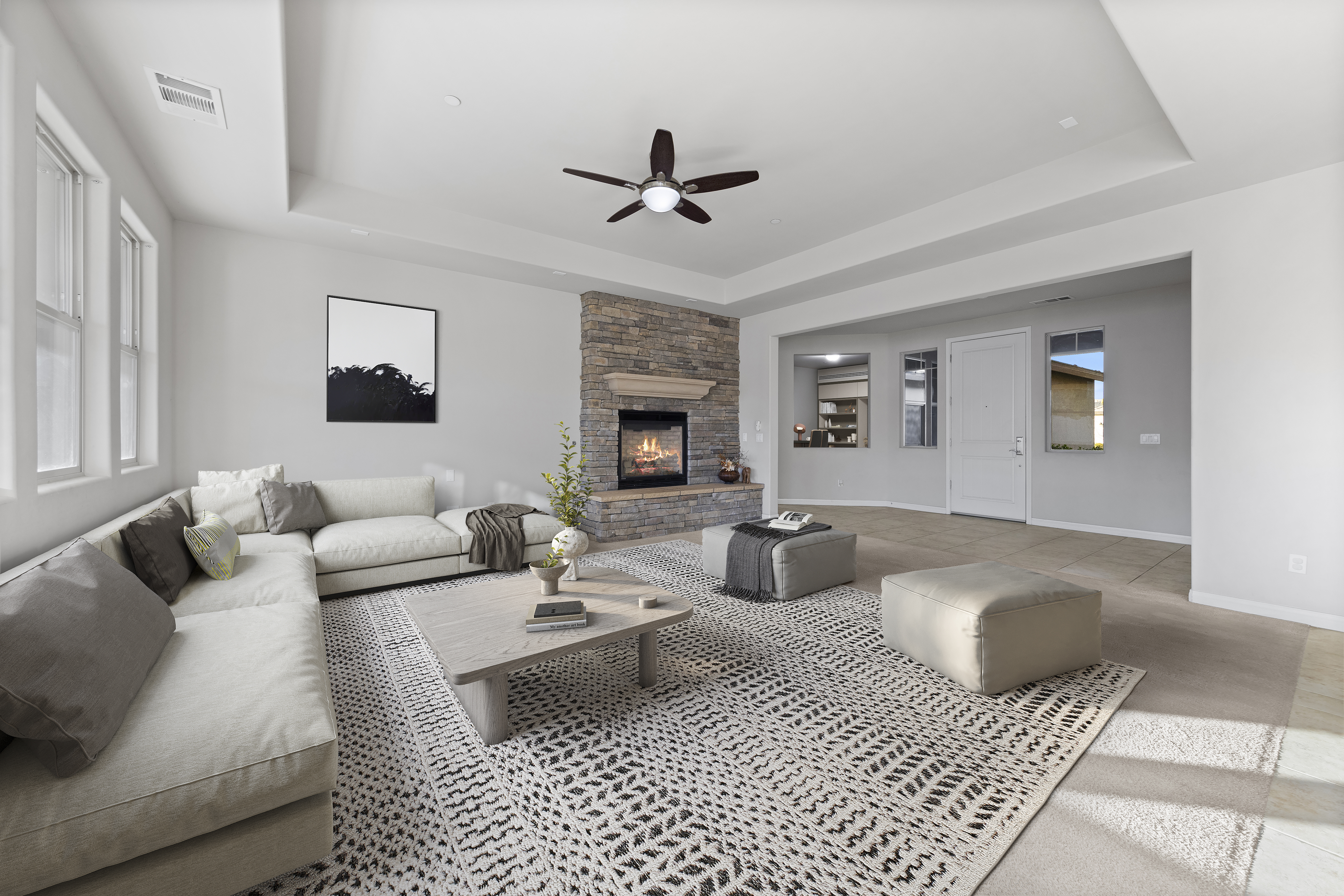 Spacious Bakersfield living room with neutral sectional sofa, stone fireplace, modern ceiling fan, and natural light, showcasing 2025 home design trends.