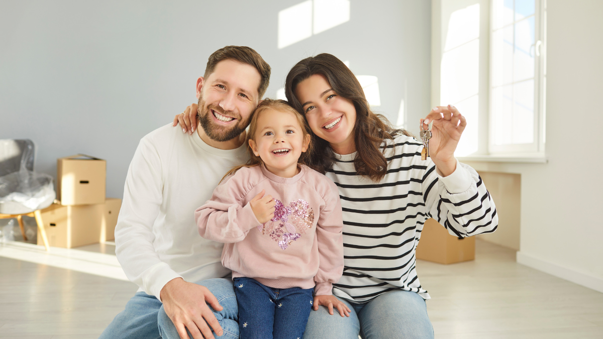 Feature image for the blog post “You’ve Bought a House, Now What?” showing a happy new homeowner holding keys in front of their house.