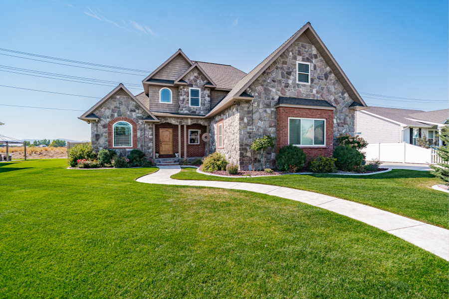 Two-story stone and brick home with manicured lawn in Idaho Falls — Elegant home featuring a stone façade, arched windows, and a curved walkway surrounded by lush green landscaping.