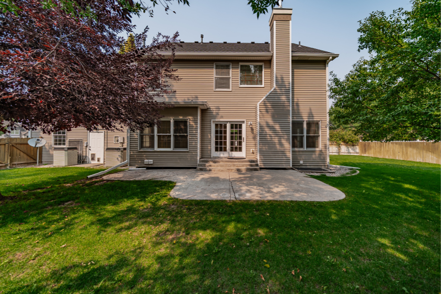 Backyard view of Idaho Falls home with patio, fenced yard, and mature trees in residential neighborhood