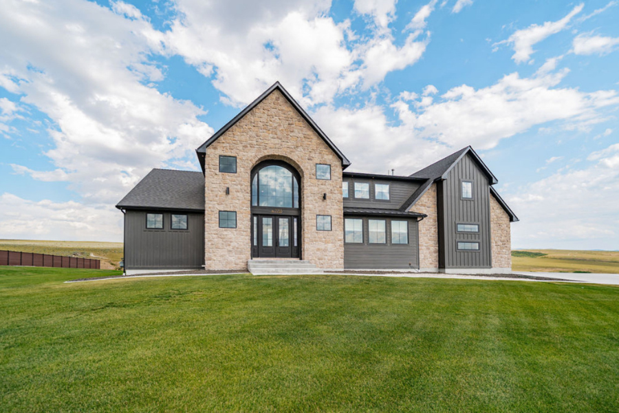 Modern farmhouse-style home with stone and dark wood exterior, located on a large green lawn under a blue sky in Idaho Falls.