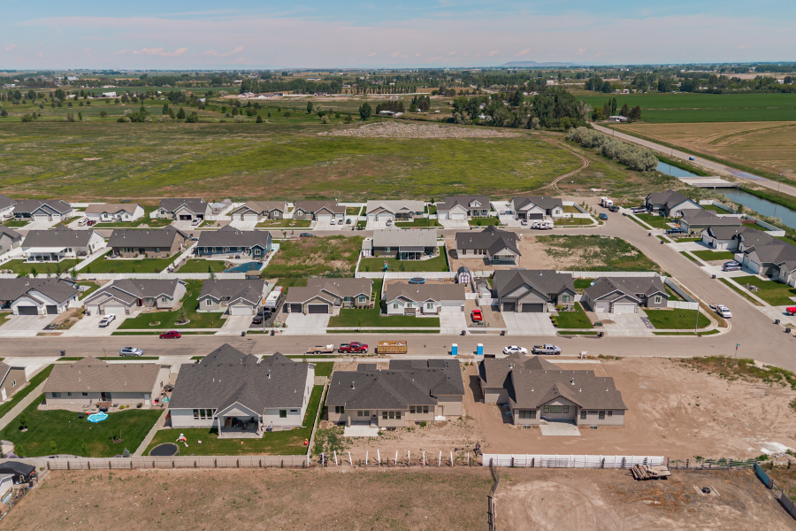Aerial view of a growing residential neighborhood with newly built homes, open lots, and surrounding farmland in Idaho Falls, Idaho.