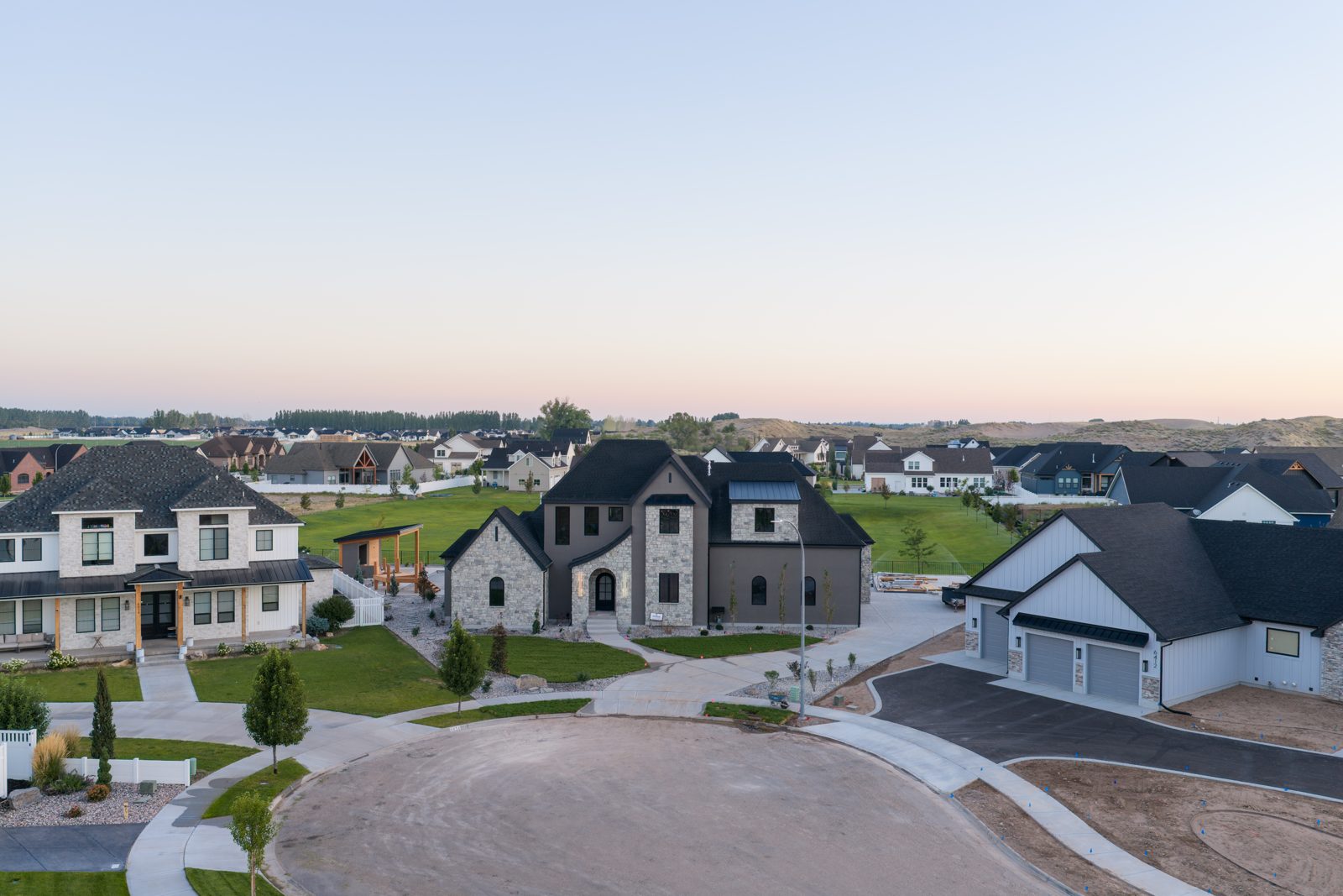 Aerial view of a cul-de-sac in an Eastern Idaho subdivision at dusk with a dark stone custom home at the center.