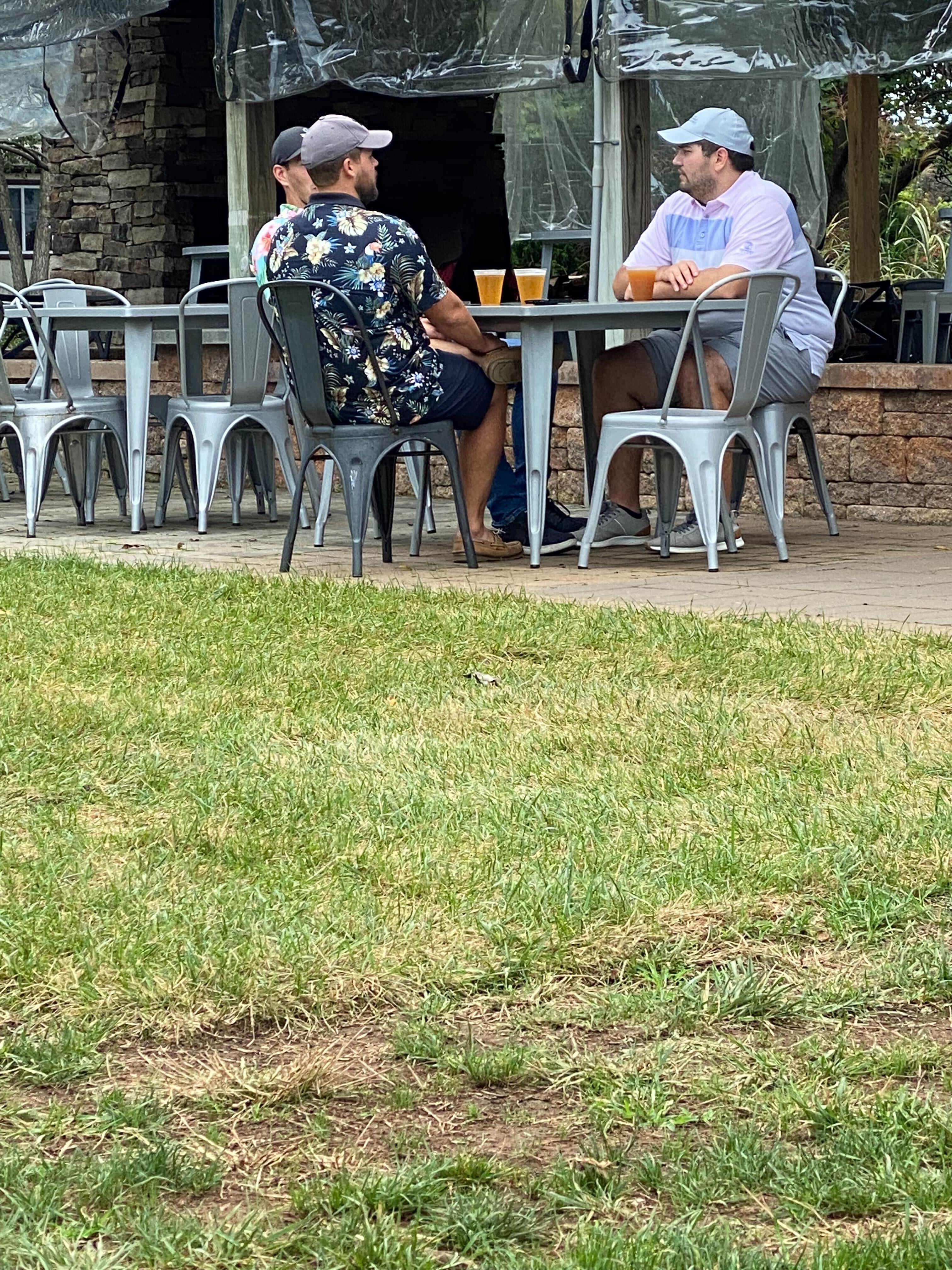 Two men relaxing and conversing at an outdoor patio table with craft beers at The Farm Brewery at Broad Run, enjoying the vibrant Northern Virginia summer ambiance.