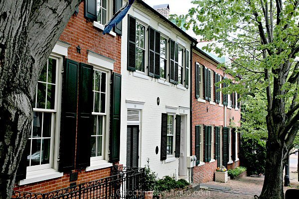 Historic colonial homes along the iconic Captain's Row on Prince Street in Old Town Alexandria, featuring classic brick facades and a tree-lined cobblestone walk.