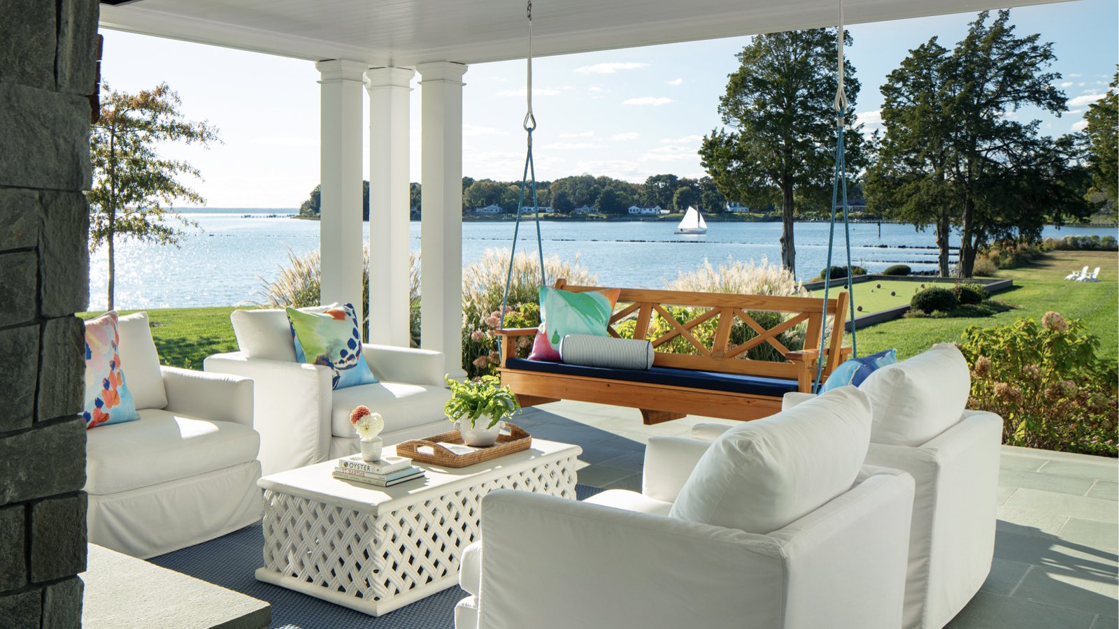 A luxurious waterfront porch with comfortable white furniture and a swing overlooking the river, showcasing the desirable outdoor lifestyle available with Virginia real estate.