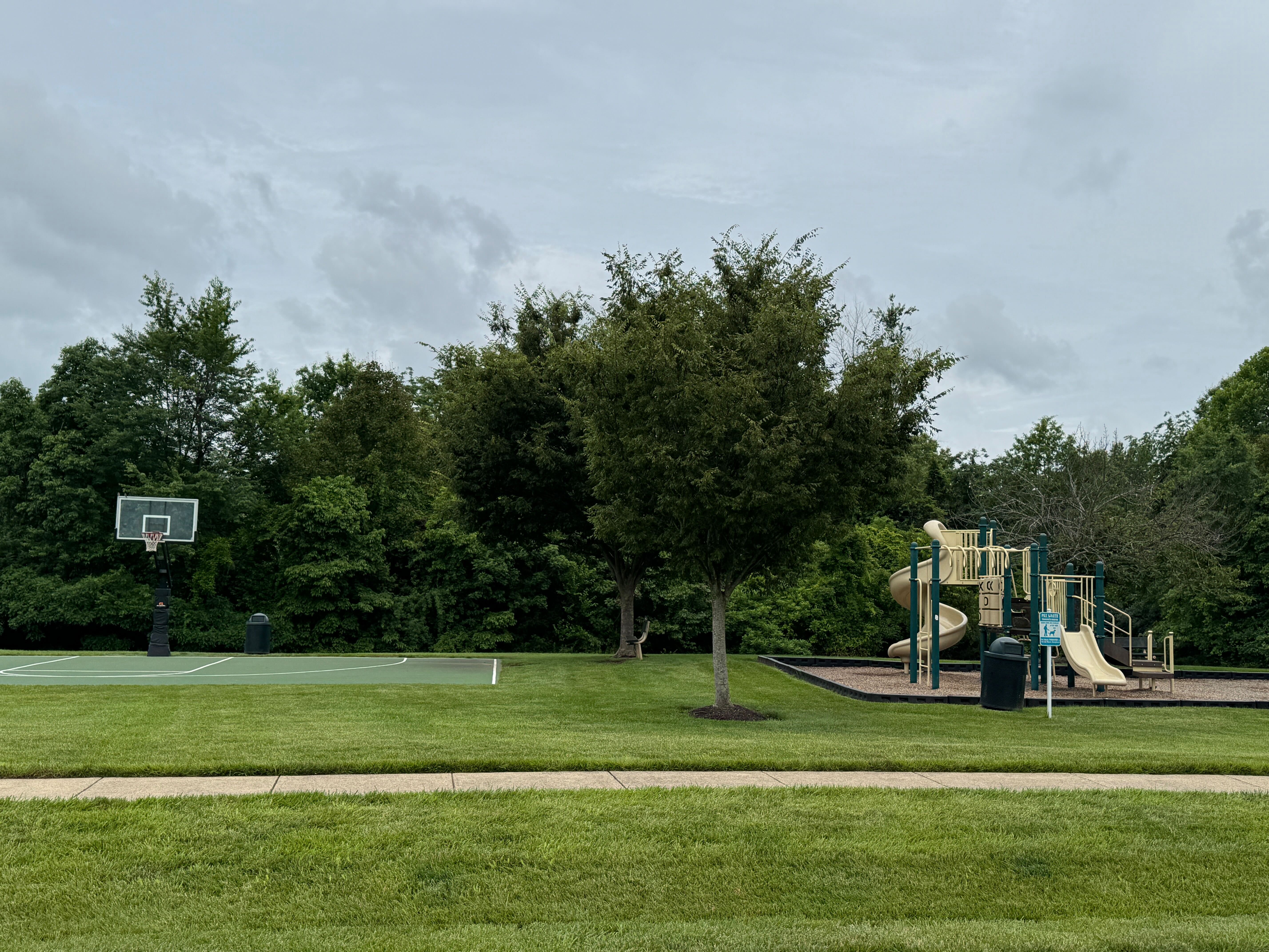 Oak Valley community park featuring a children's playground, basketball court, and open green space under an overcast sky.