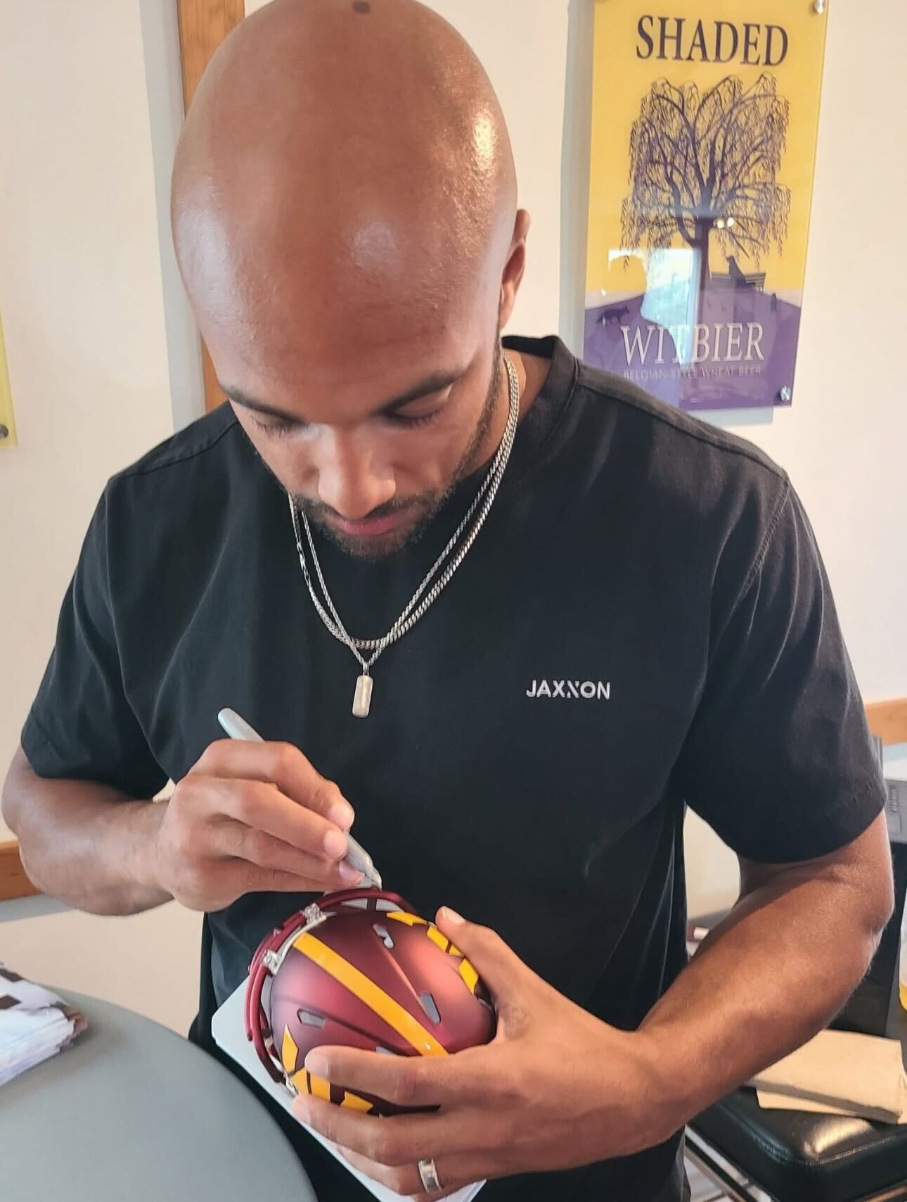 Washington Commanders running back Austin Ekeler signing an autograph on a mini helmet at the Colgan Team client appreciation event.
