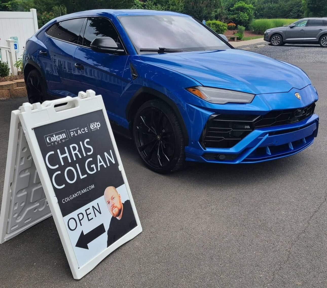 A blue Lamborghini Urus parked next to a Colgan Team real estate A-frame sign for agent Chris Colgan.