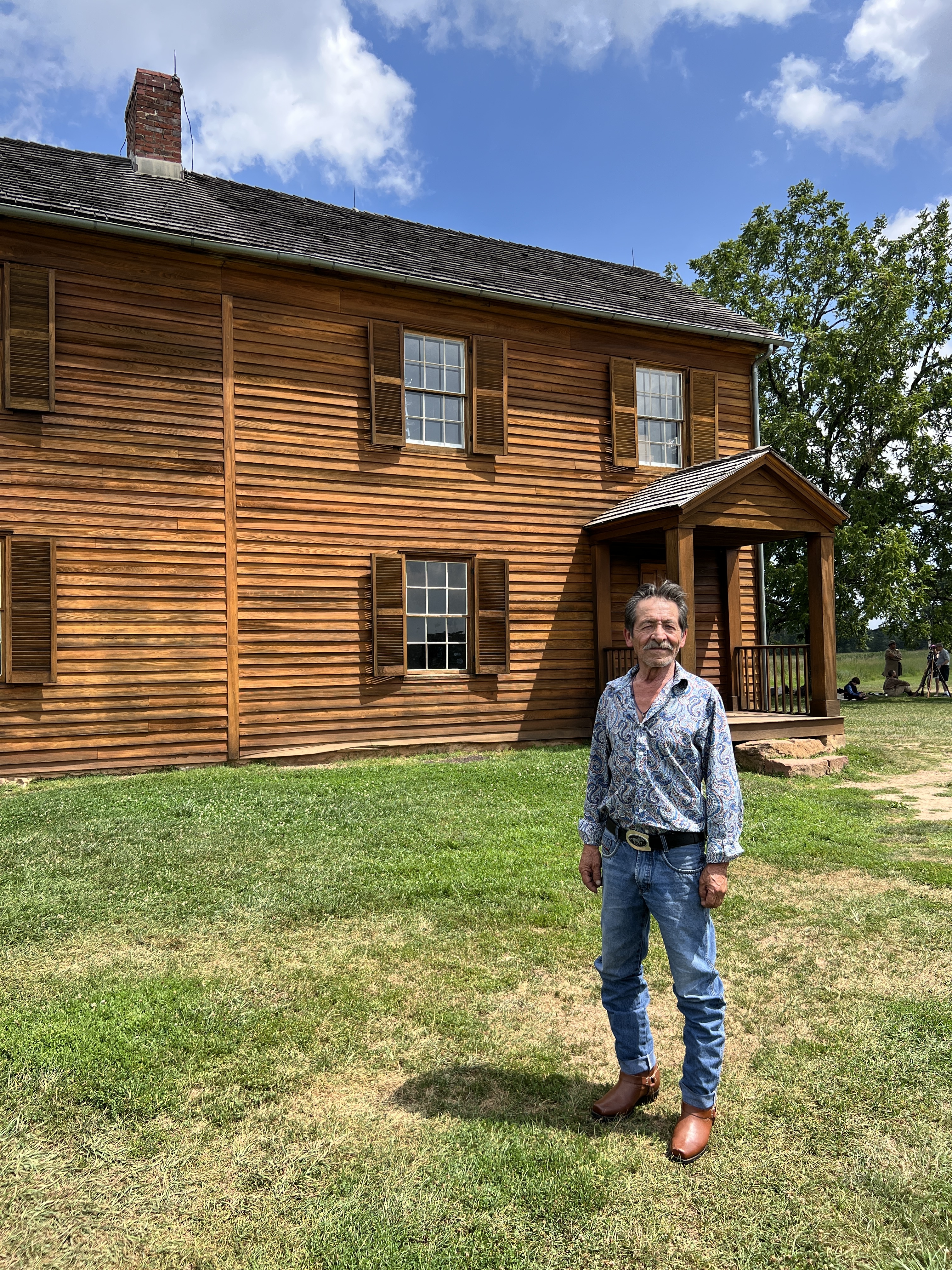 The historic Henry House, a key landmark on the battlefield, with a visitor posing in the foreground on a sunny day.