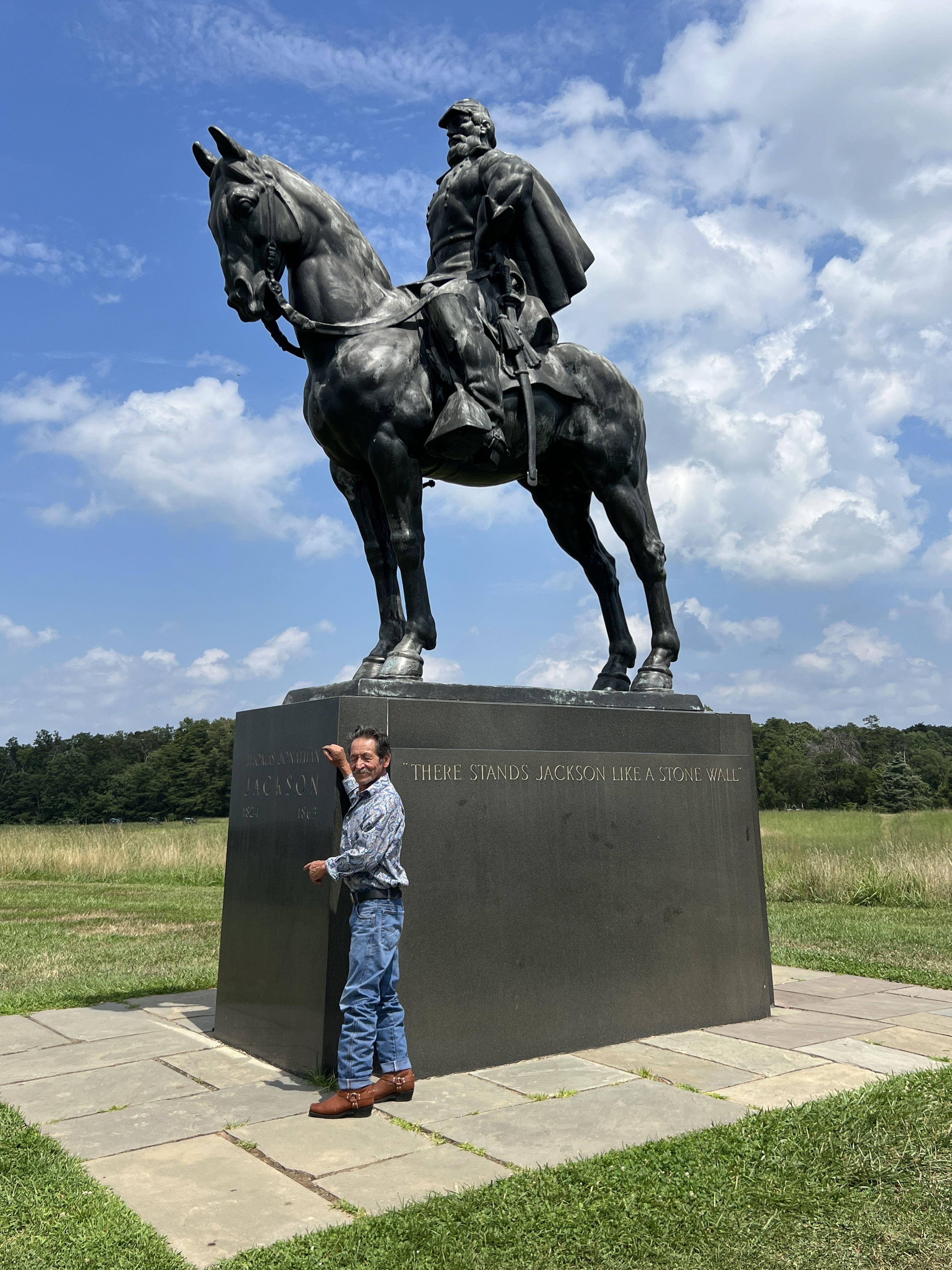 The Stonewall Jackson monument at Manassas, with a visitor touching the plinth where the quote 'There stands Jackson like a stone wall' is inscribed.
