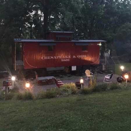 The historic Chesapeake & Ohio train caboose Airbnb at dusk in Natural Bridge, Virginia, with warm lights illuminating the cozy outdoor seating area.