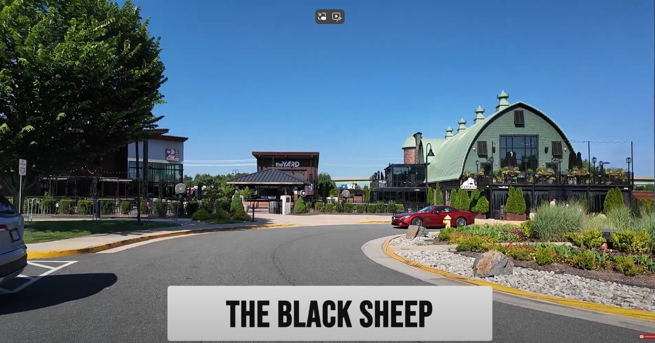 A sunny daytime view of the entrance to The Yard at Fishers District, home to The Black Sheep restaurant and its unique green barn architecture.