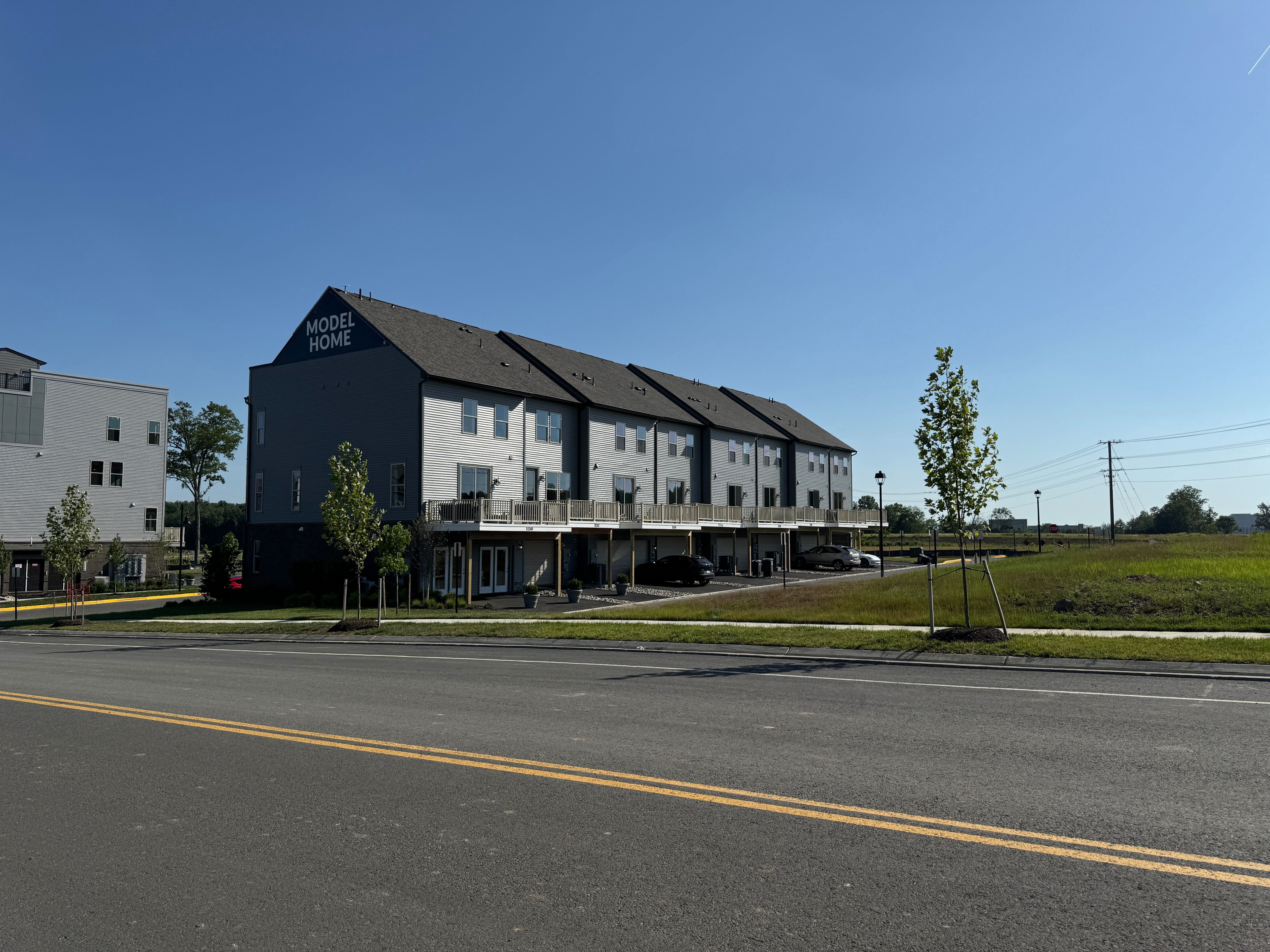 A street view of the finished Stanley Martin model townhome, a modern grey building with a second-story balcony, at Innovation Town Center in Manassas, VA.