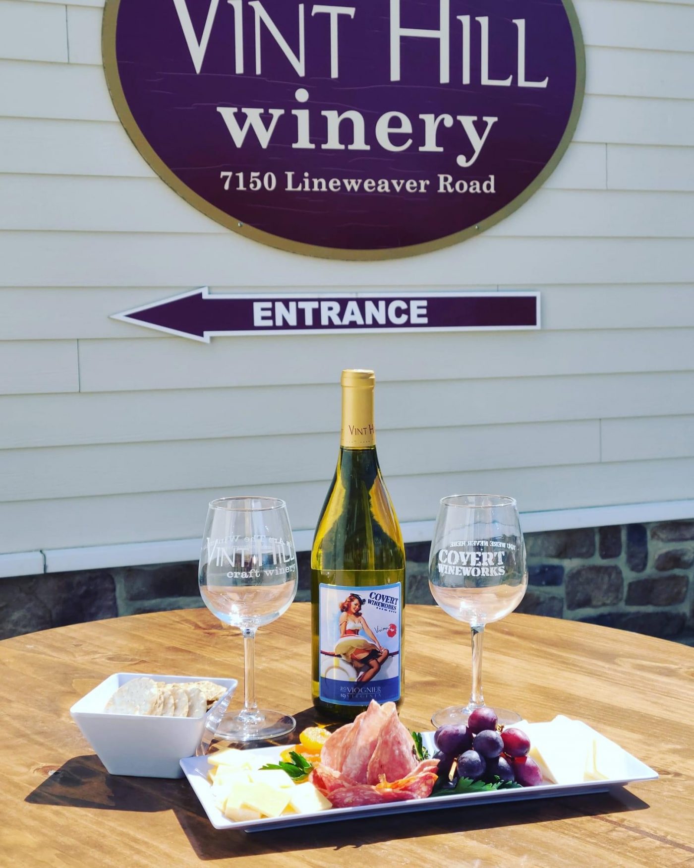 A wine tasting experience at Vint Hill Winery with a bottle of Covert Vineworks wine, two glasses, and a charcuterie board on an outdoor table.