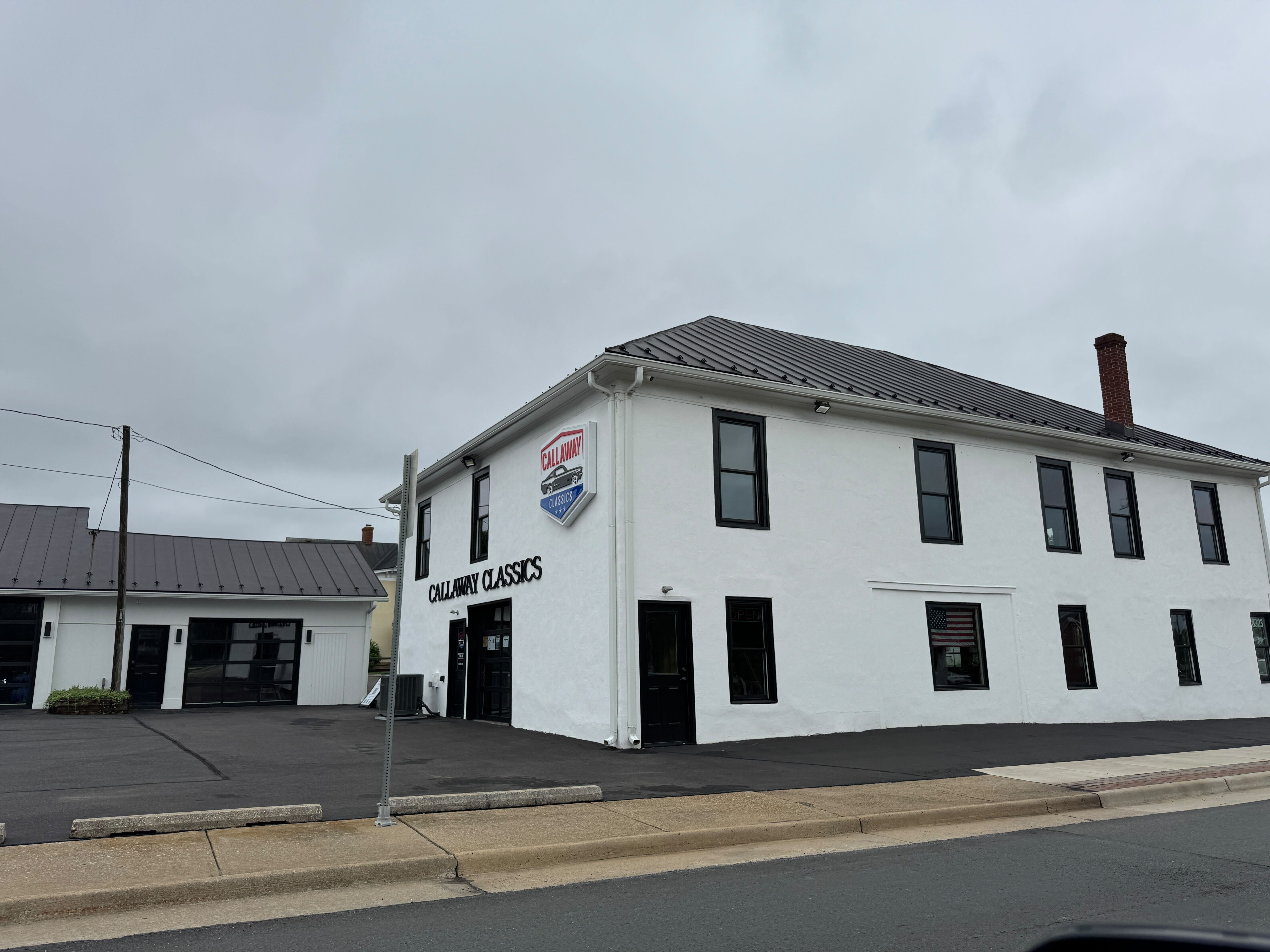 The clean, modern exterior of Callaway Classics in Warrenton, VA, a white building with black trim that houses a classic and exotic car dealership.