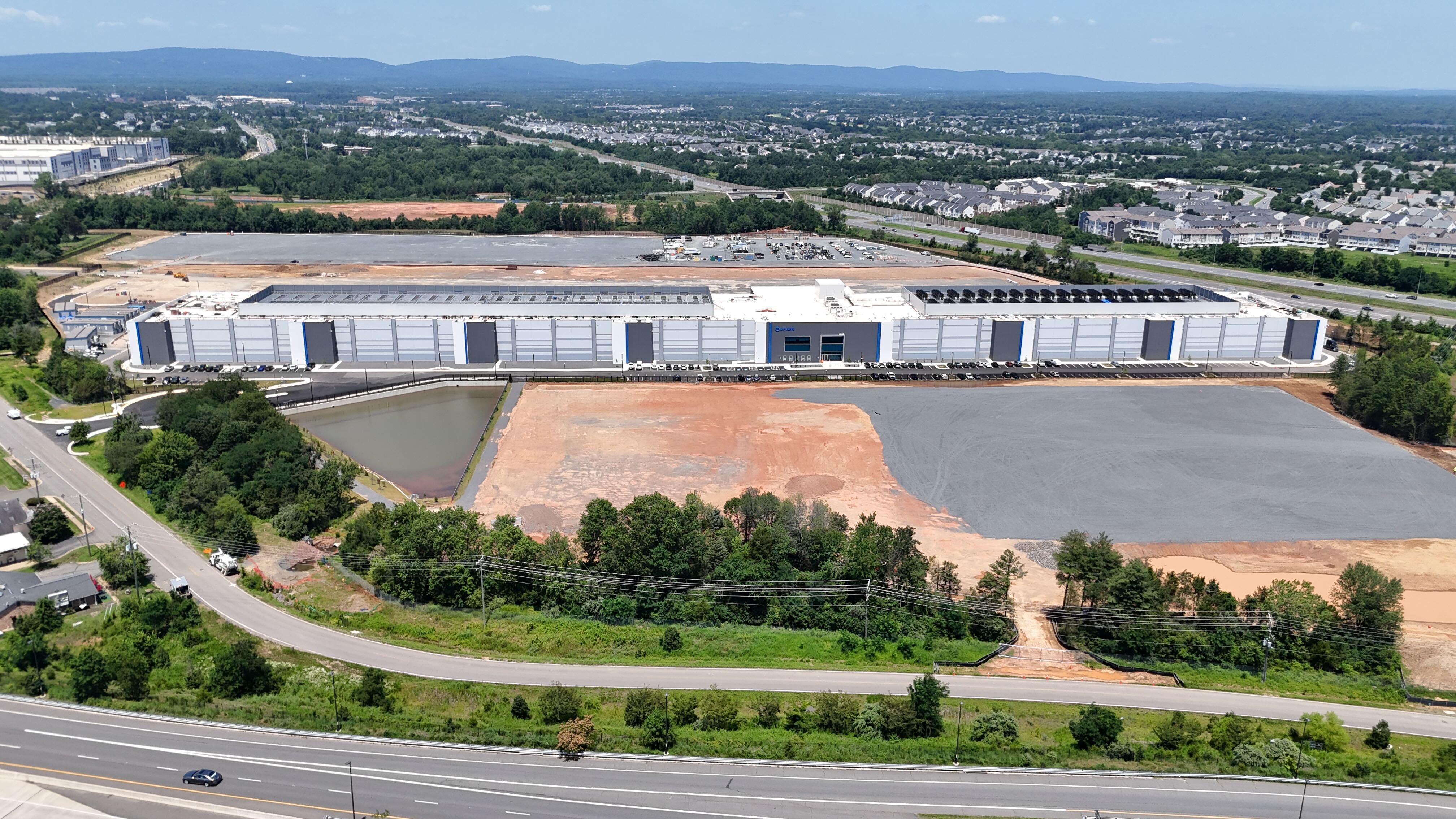 Aerial view of a large data center under construction in Gainesville, Virginia, showing the massive building, retention ponds, and surrounding development.