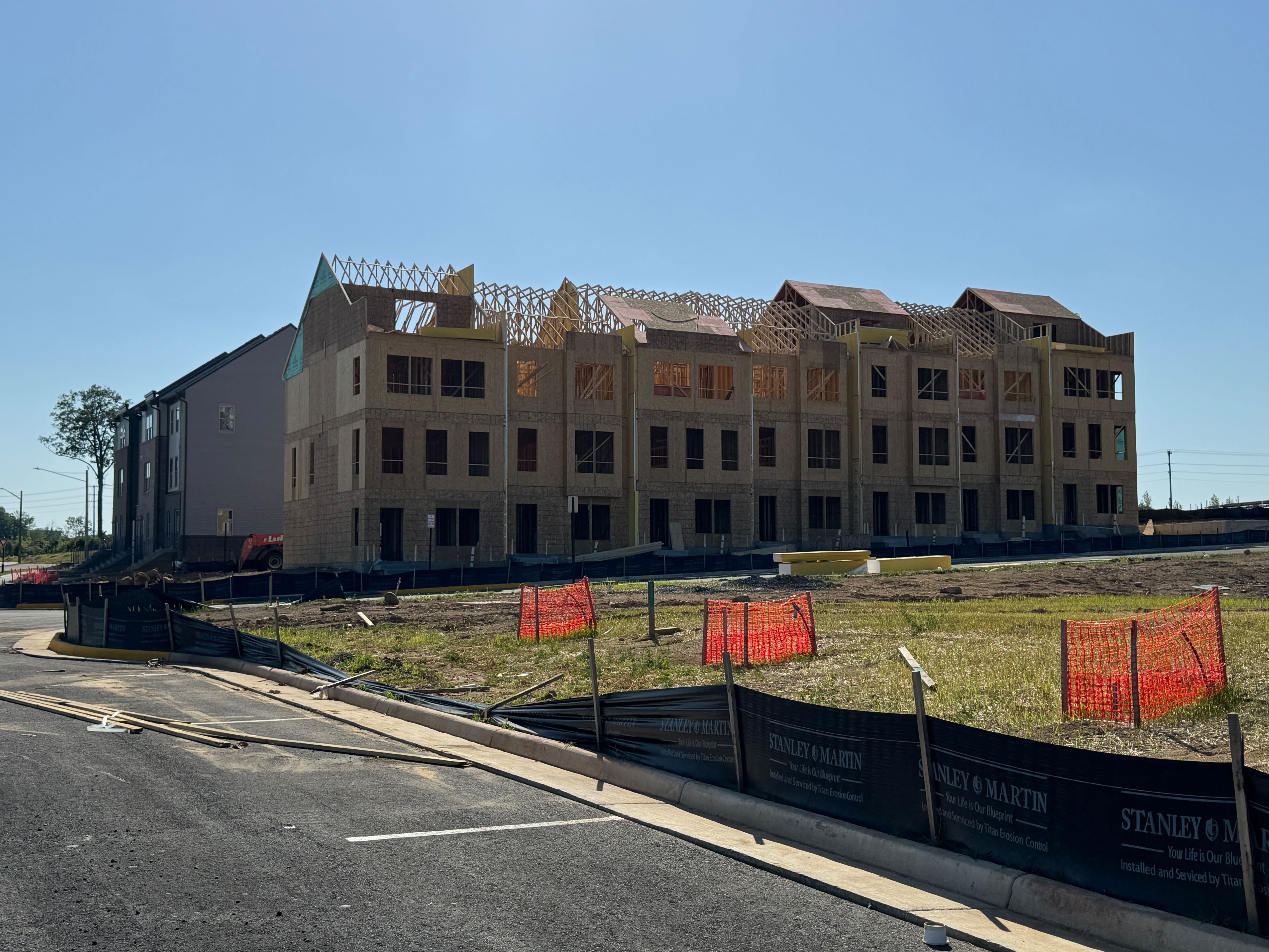 A ground-level view of a new Stanley Martin townhome building under construction at Innovation Town Center, showing the wood framing and roof trusses.