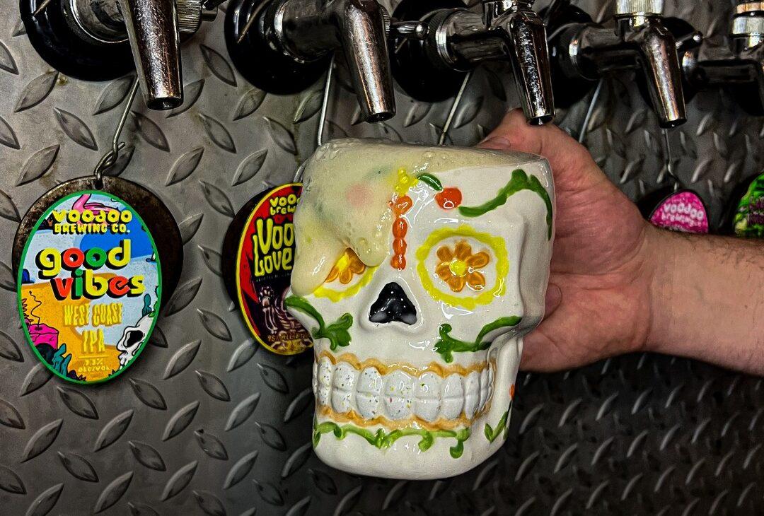The unique pub experience at Voodoo Brewing Co., featuring one of their signature sugar skull mugs filled with fresh craft beer on tap.