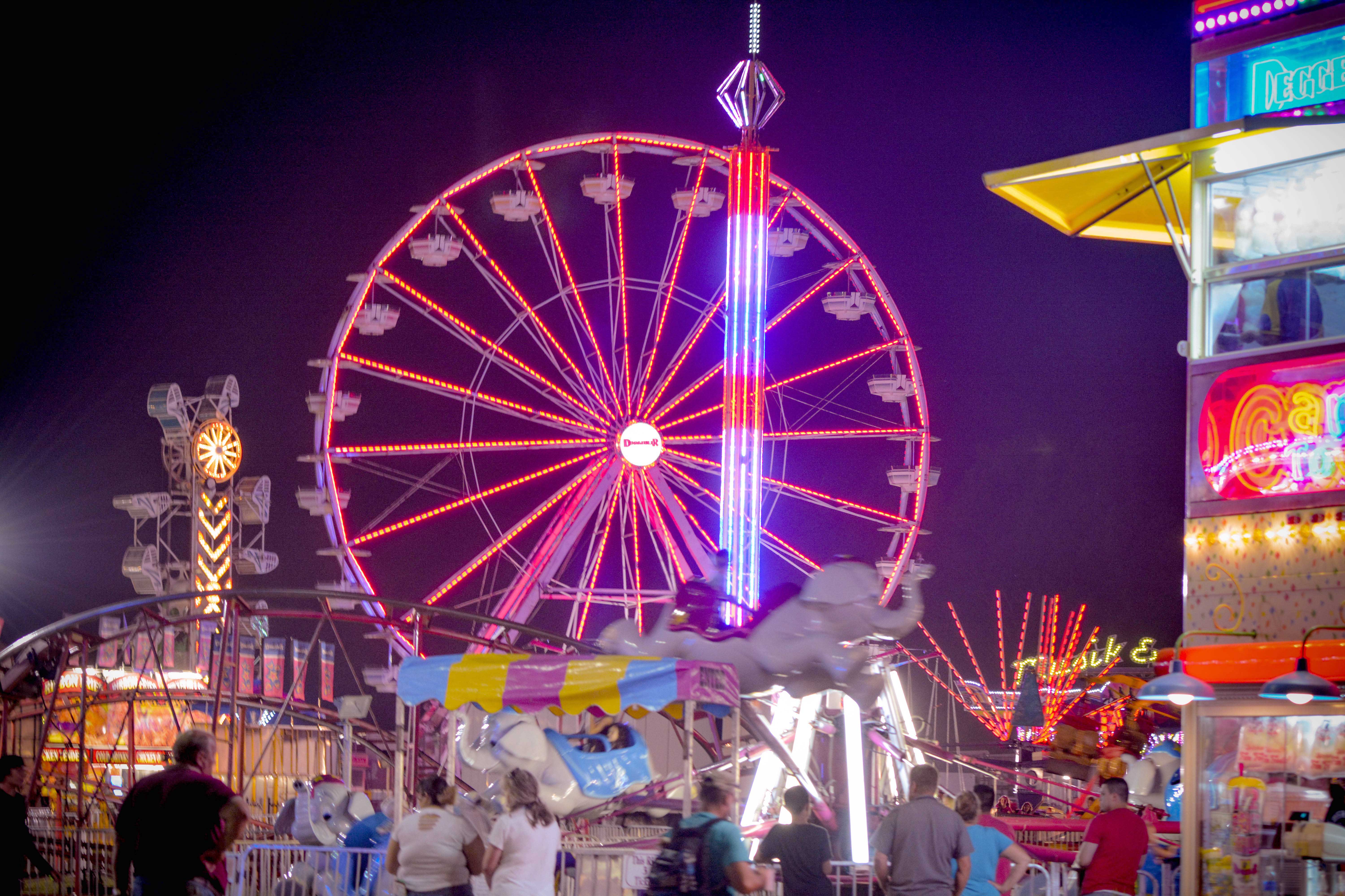 The Fredericksburg County Fair illuminated at night, with a large Ferris wheel and other carnival rides glowing as people enjoy the festivities.