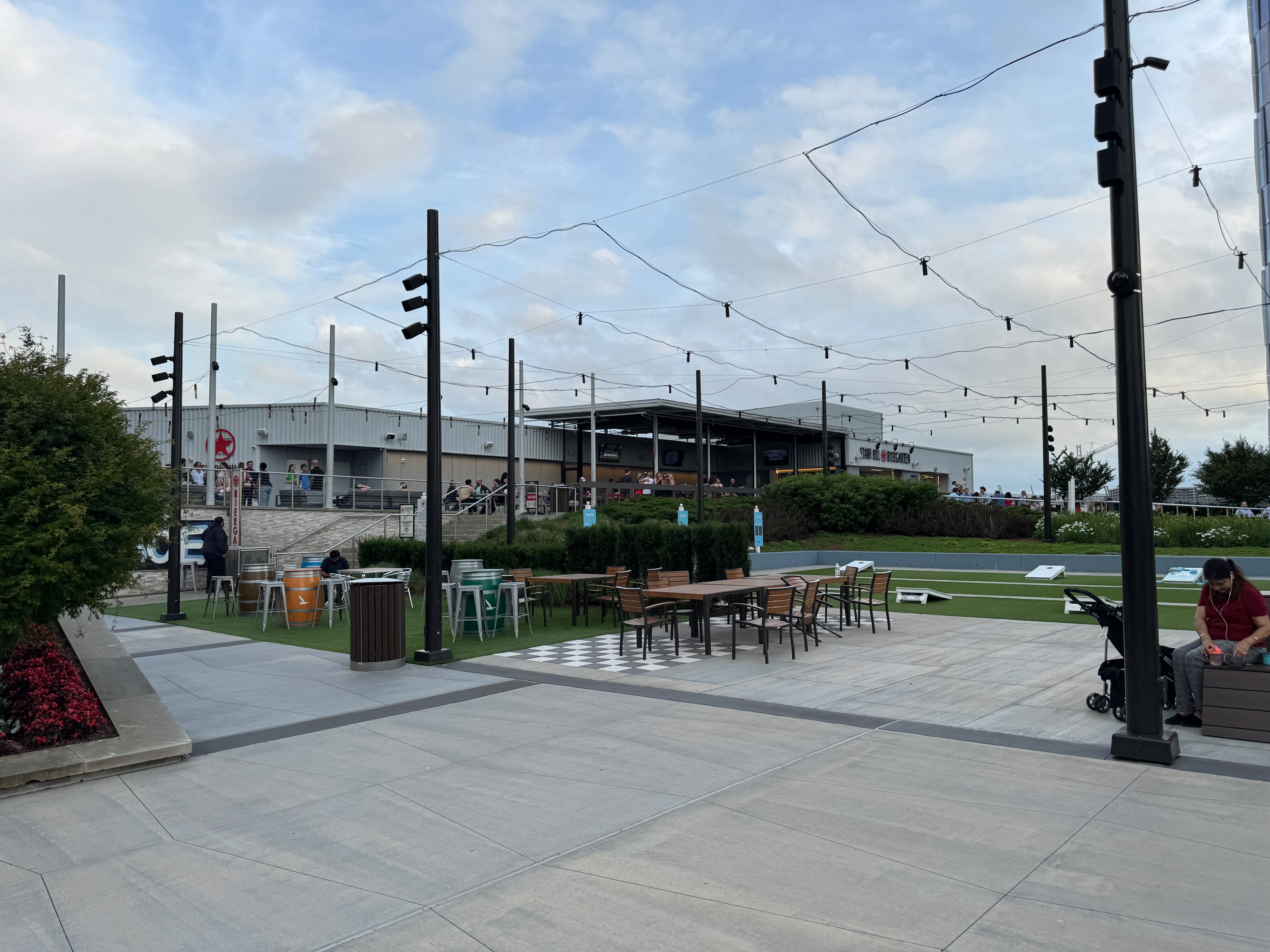 The spacious main plaza at The Perch in Tysons, featuring a large artificial turf lawn with a cornhole game, various outdoor seating areas, and the Starr Hill Biergarten in the background.