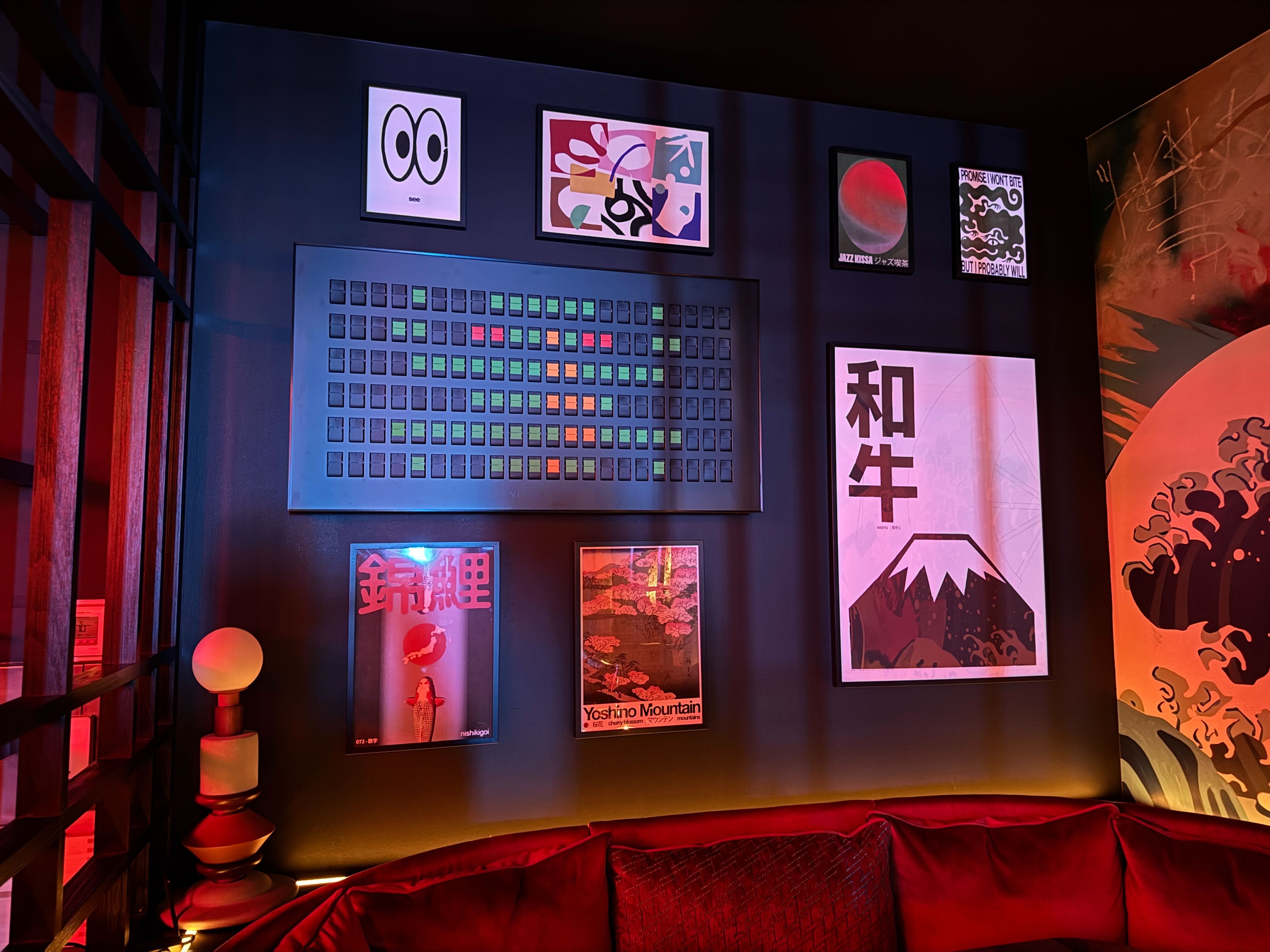 The curated gallery wall inside Naisō Room in Tysons, featuring a mix of modern and Japanese-themed art, a large kinetic display, and a plush red velvet sofa.