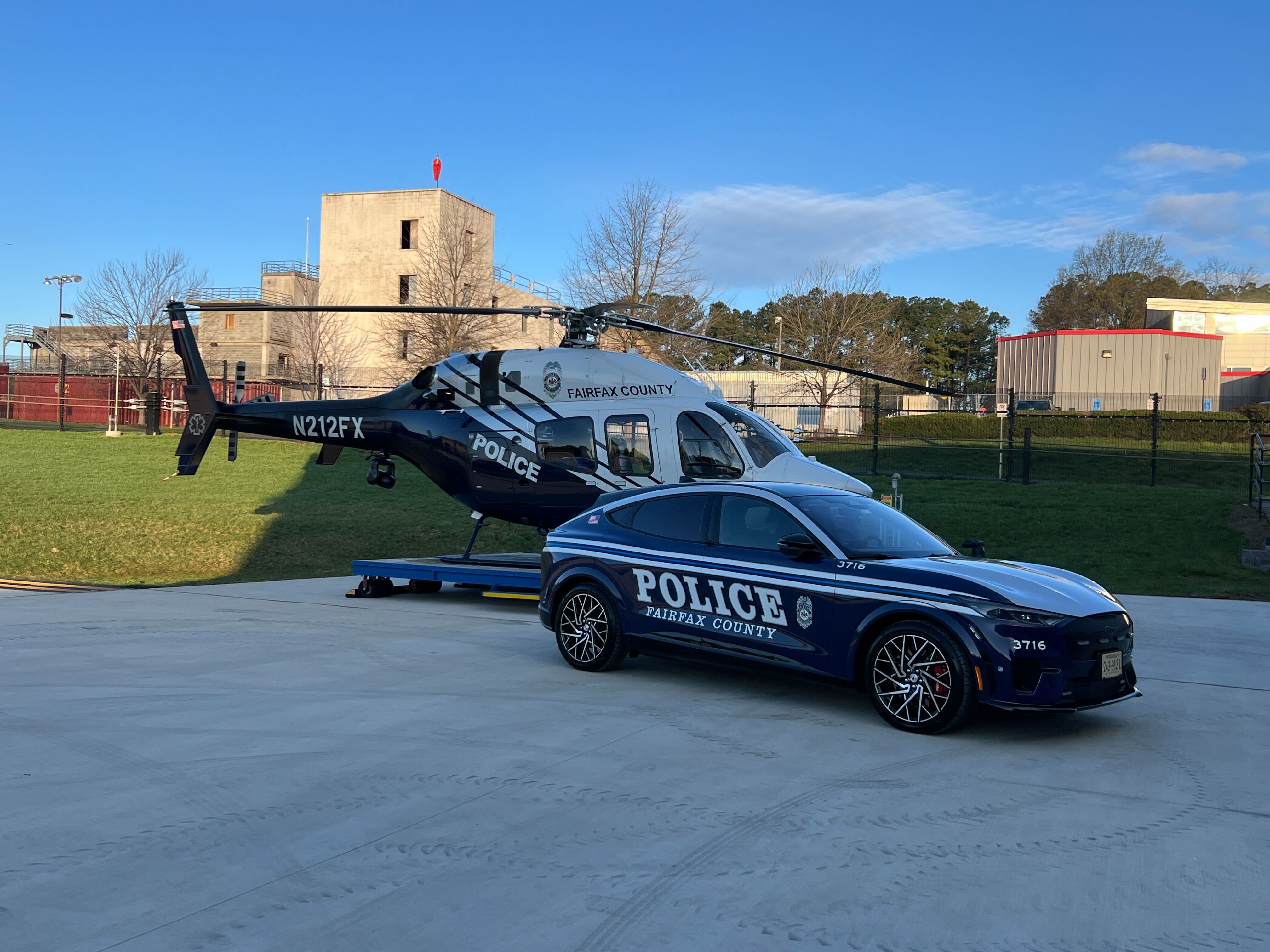 A Fairfax County Police Ford Mustang Mach-E patrol car parked in front of a police helicopter on a landing pad.