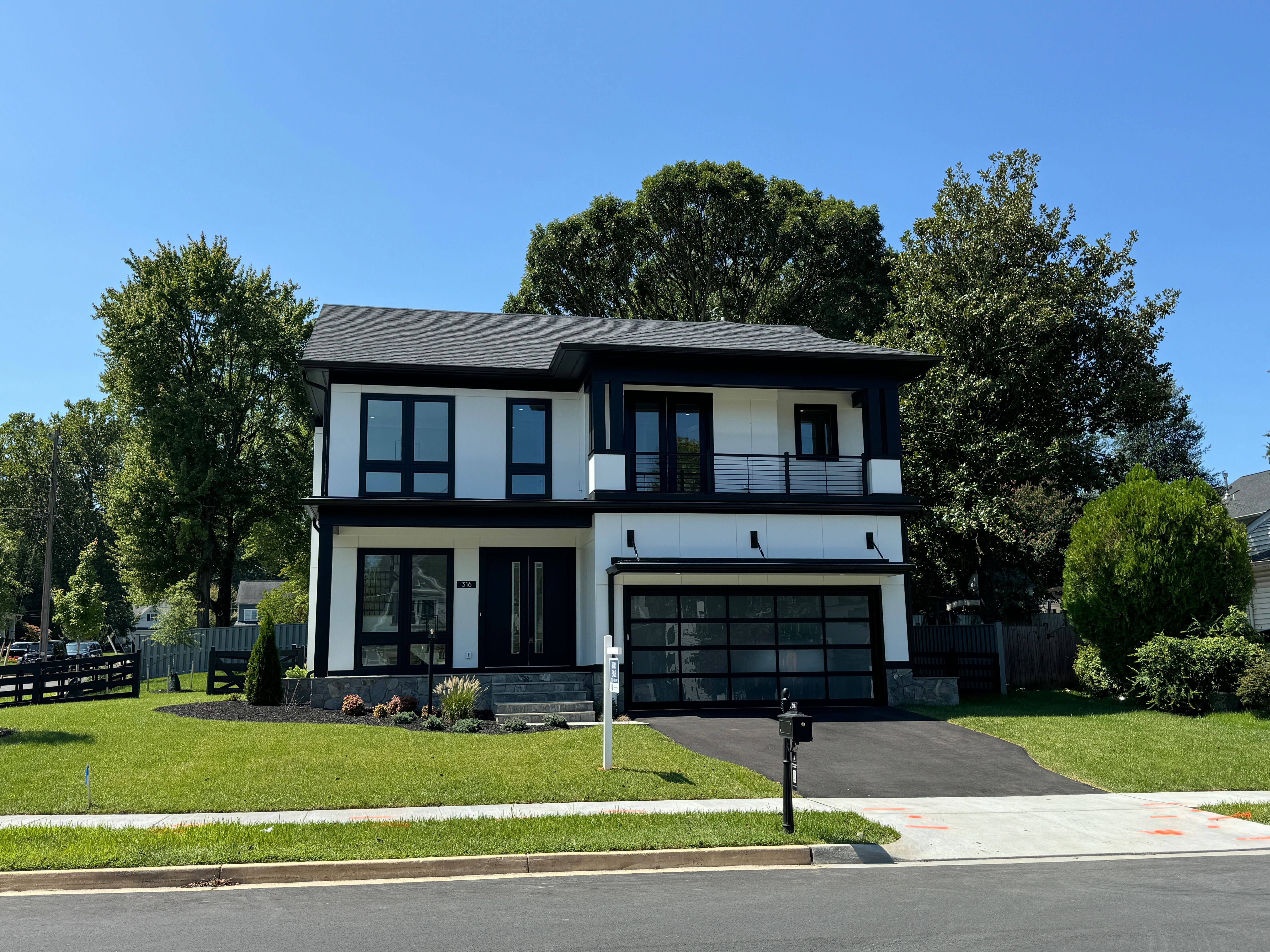 The exterior of a modern two-story home with a black and white facade, a second-floor balcony, and a glass-paneled garage door.