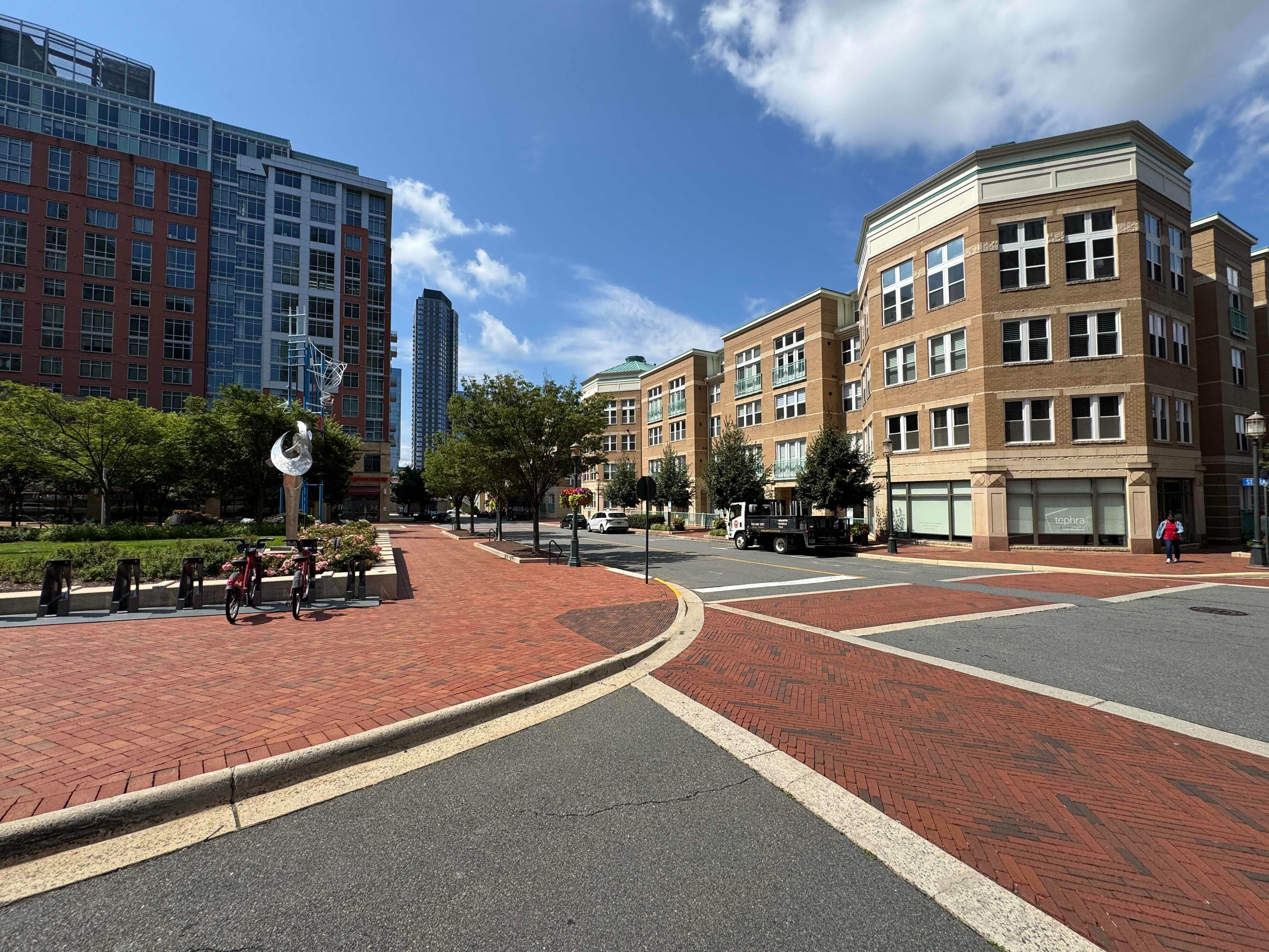 A sweeping street view of Reston Town Center's plaza, showing the red brick walkways, modern architecture, public art, and a Capital Bikeshare station.
