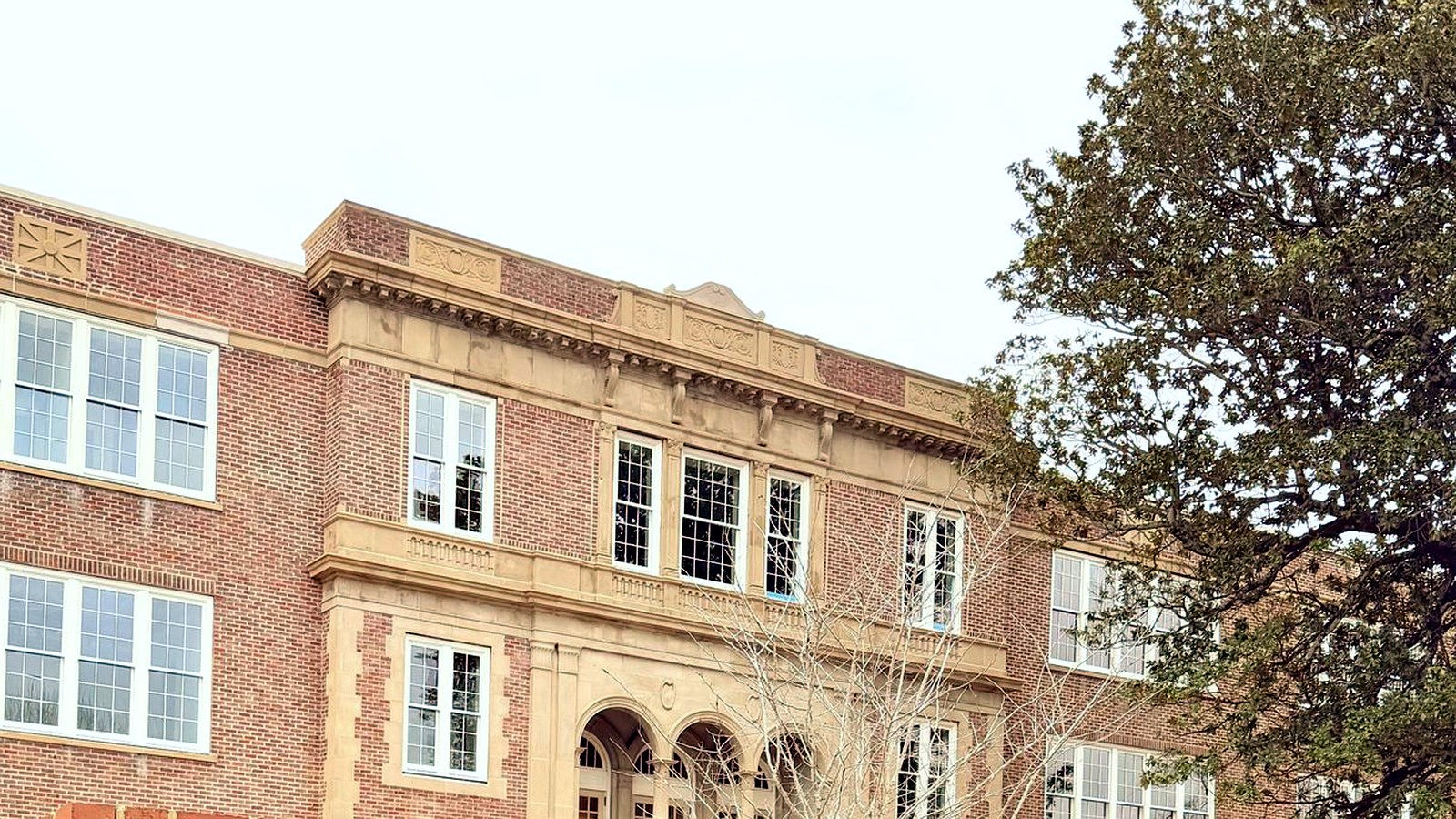 A 1920s brick and limestone landmark building framed by mature oaks near the Twickenham Historic District in downtown Huntsville, Alabama