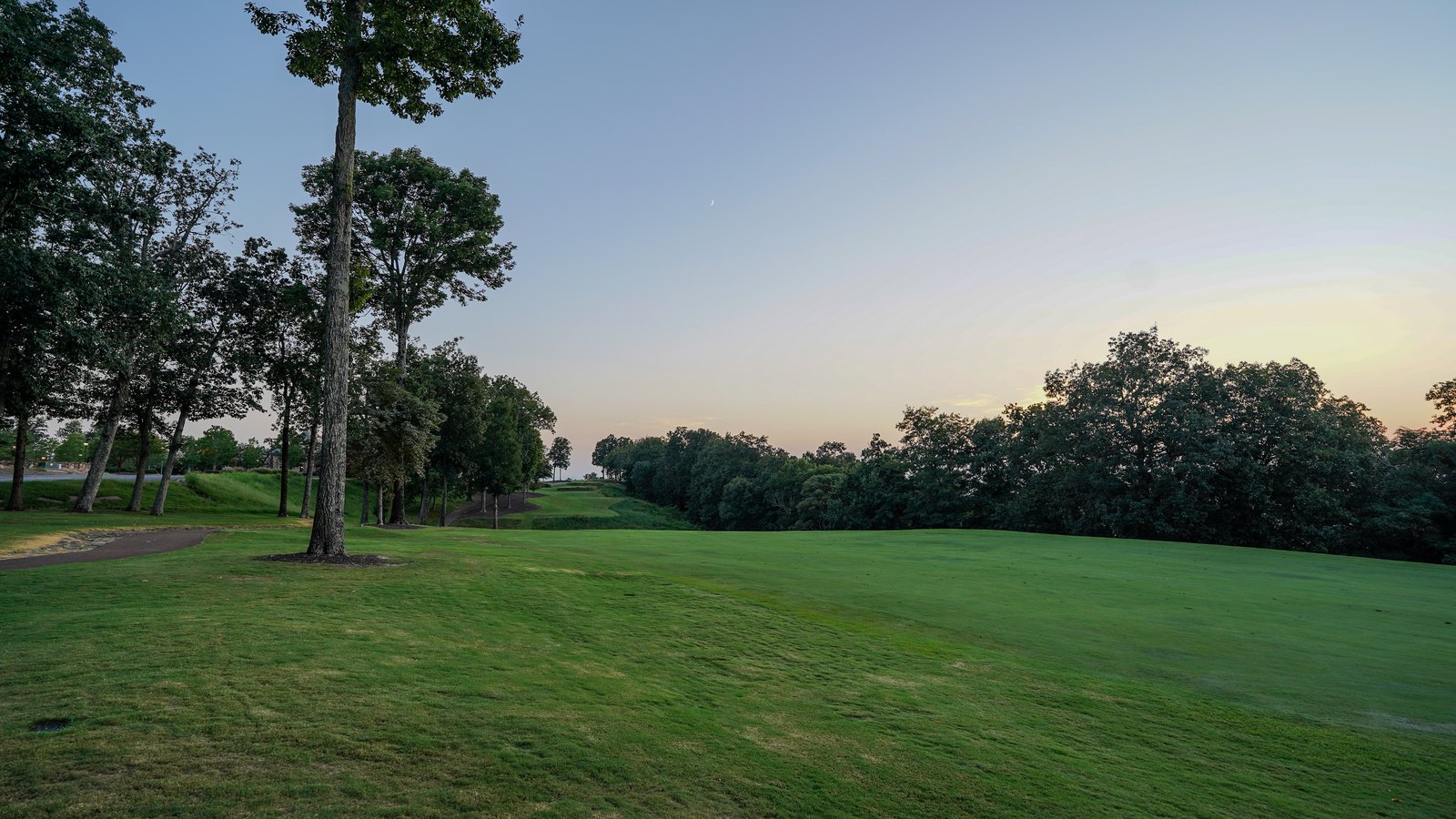A golf fairway at dusk under a crescent moon, framed by trees on the mountain above Huntsville, Alabama, at The Ledges
