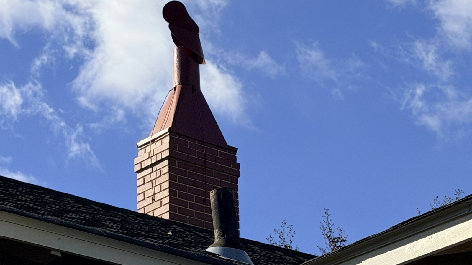 A brick chimney and shingle roofline against a blue sky on a Huntsville, Alabama home
