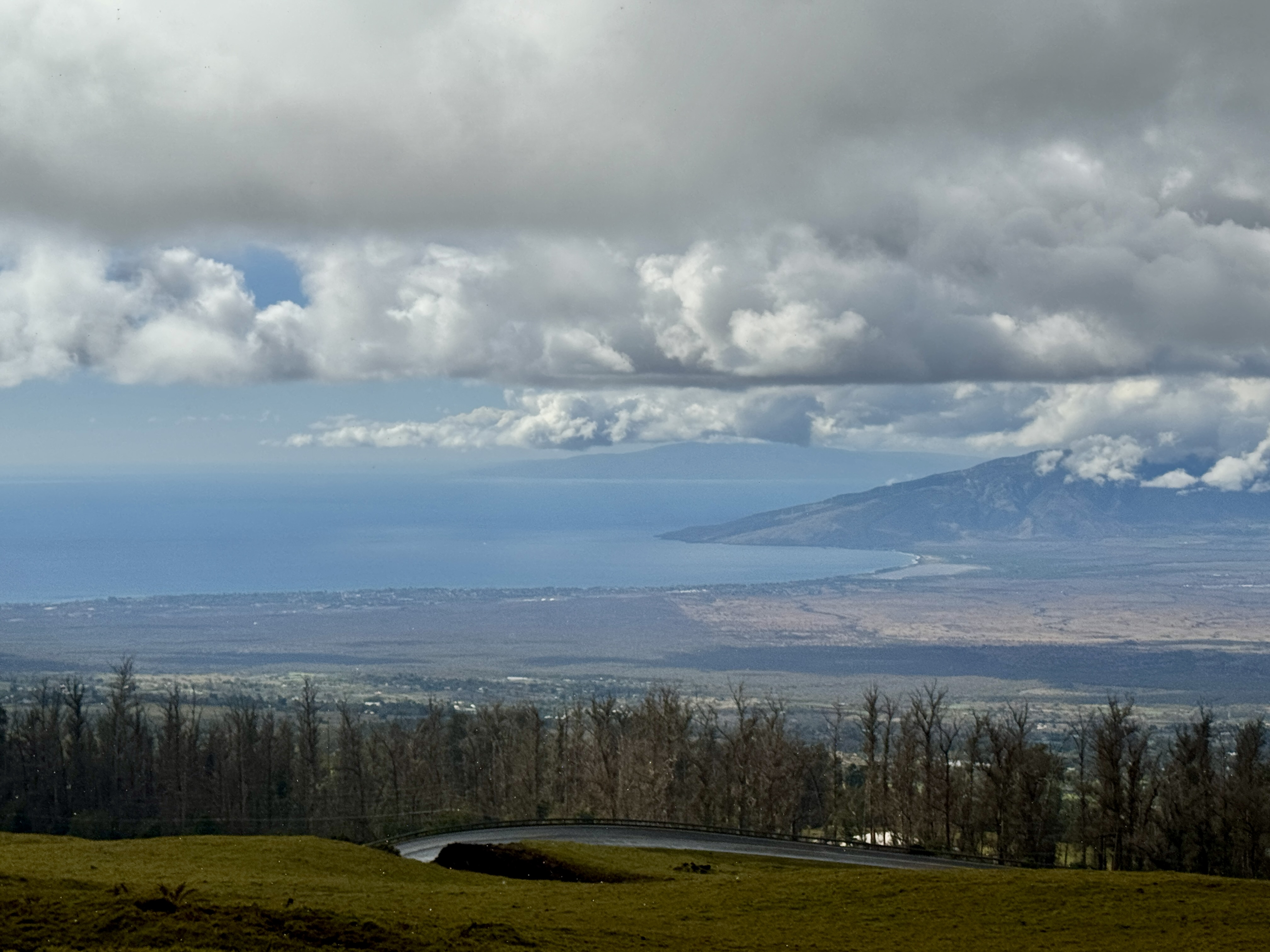 Lush green pastures and rolling hills in Upcountry Maui with distant views of Haleakala and scattered homes nestled in the landscape