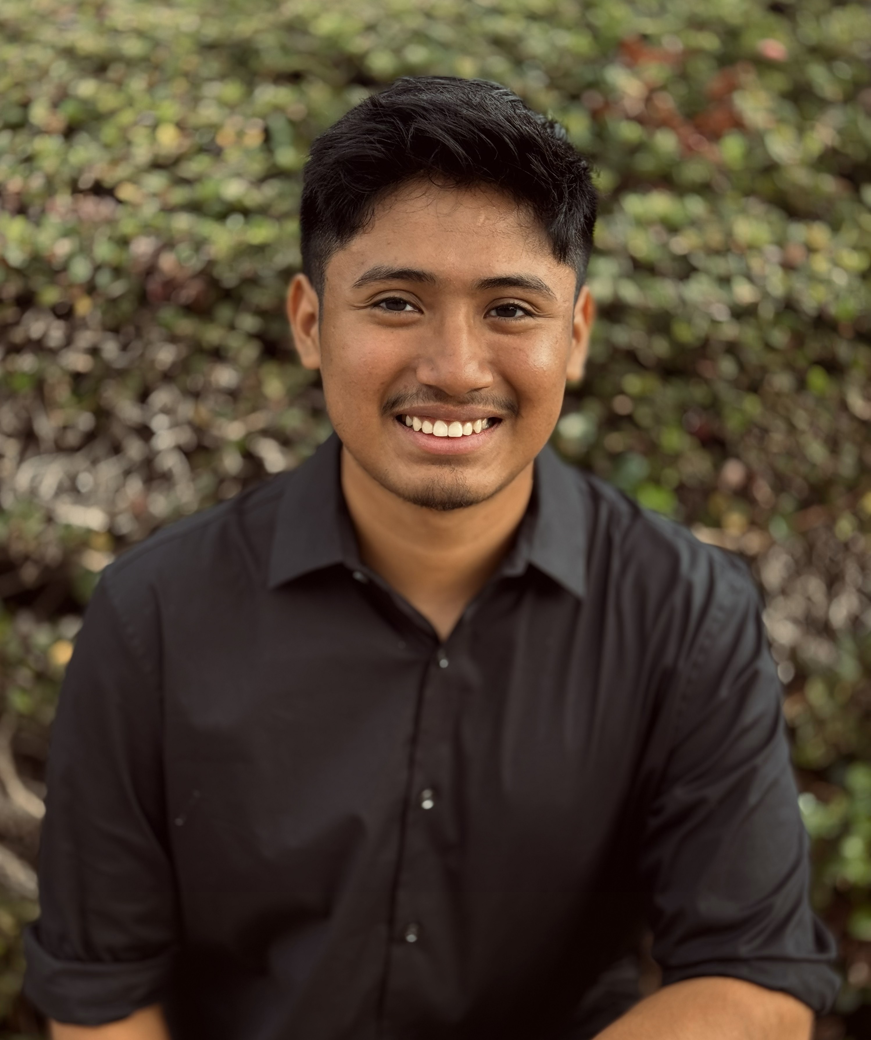 Portrait of Francisco, a 19-year-old Maui Realtor with The 808 Team, smiling outdoors in a black button-down shirt.