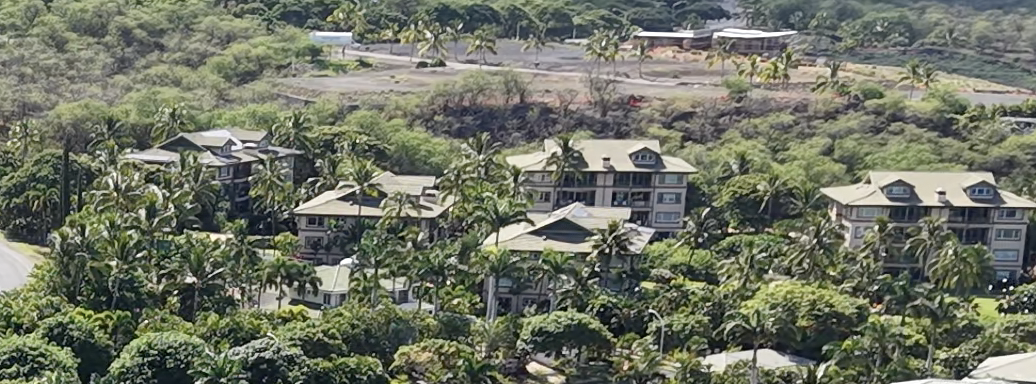 Aerial view of Na Hale O Makena luxury residential condominium community in Makena, South Maui, showing multi-story plantation-style buildings surrounded by dense tropical palms and lush green hillside vegetation.
