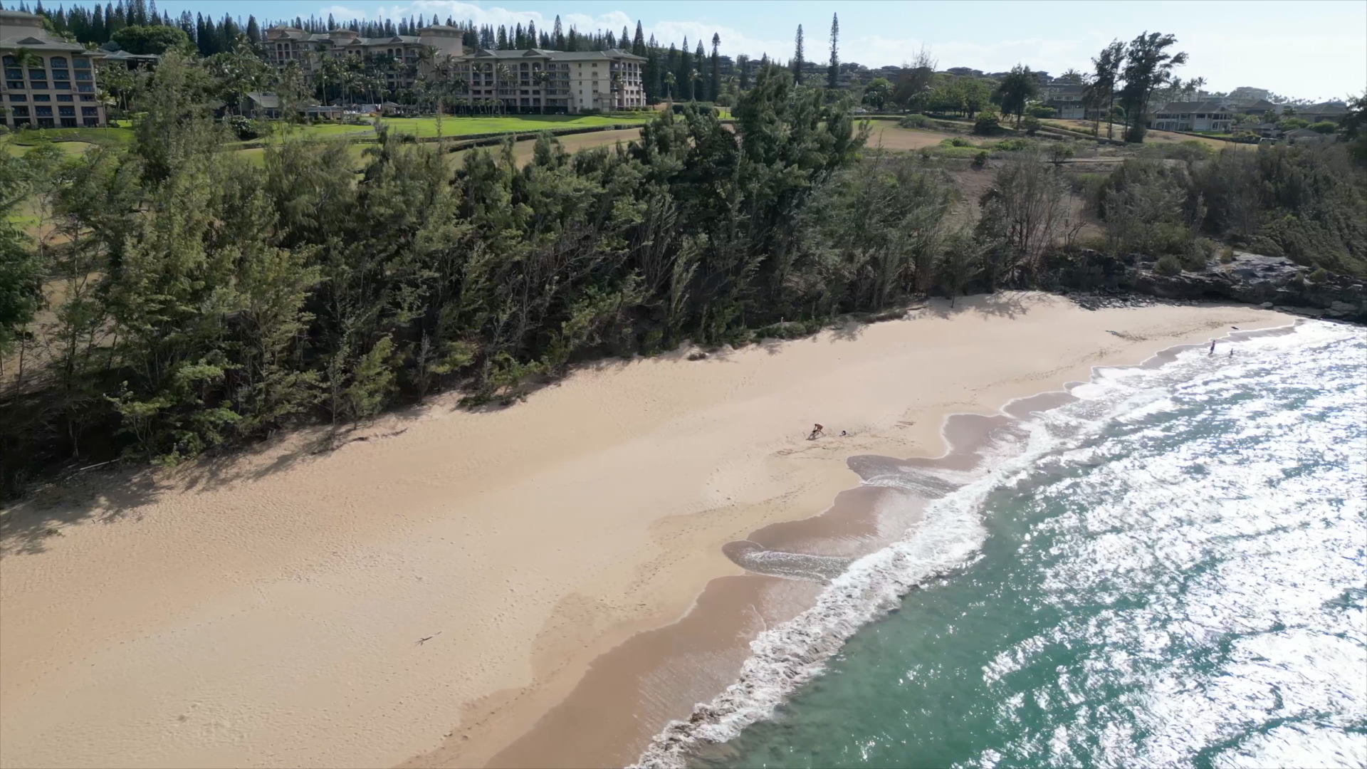 Scenic view of DT Fleming Beach Park in West Maui with golden sand, blue ocean, and lush greenery under a clear sky.