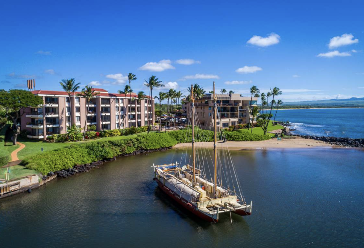 Maalaea Yacht Marina condominiums in Maalaea, Maui overlooking Maalaea Harbor with boats, ocean views, palm trees, and West Maui Mountains in the background