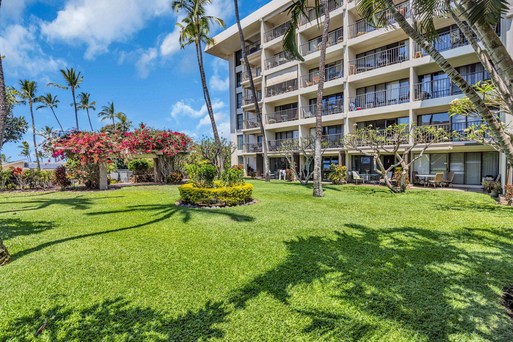 Front of the Kihei Akahi condominium building in Kihei, with palm trees and a green lawn