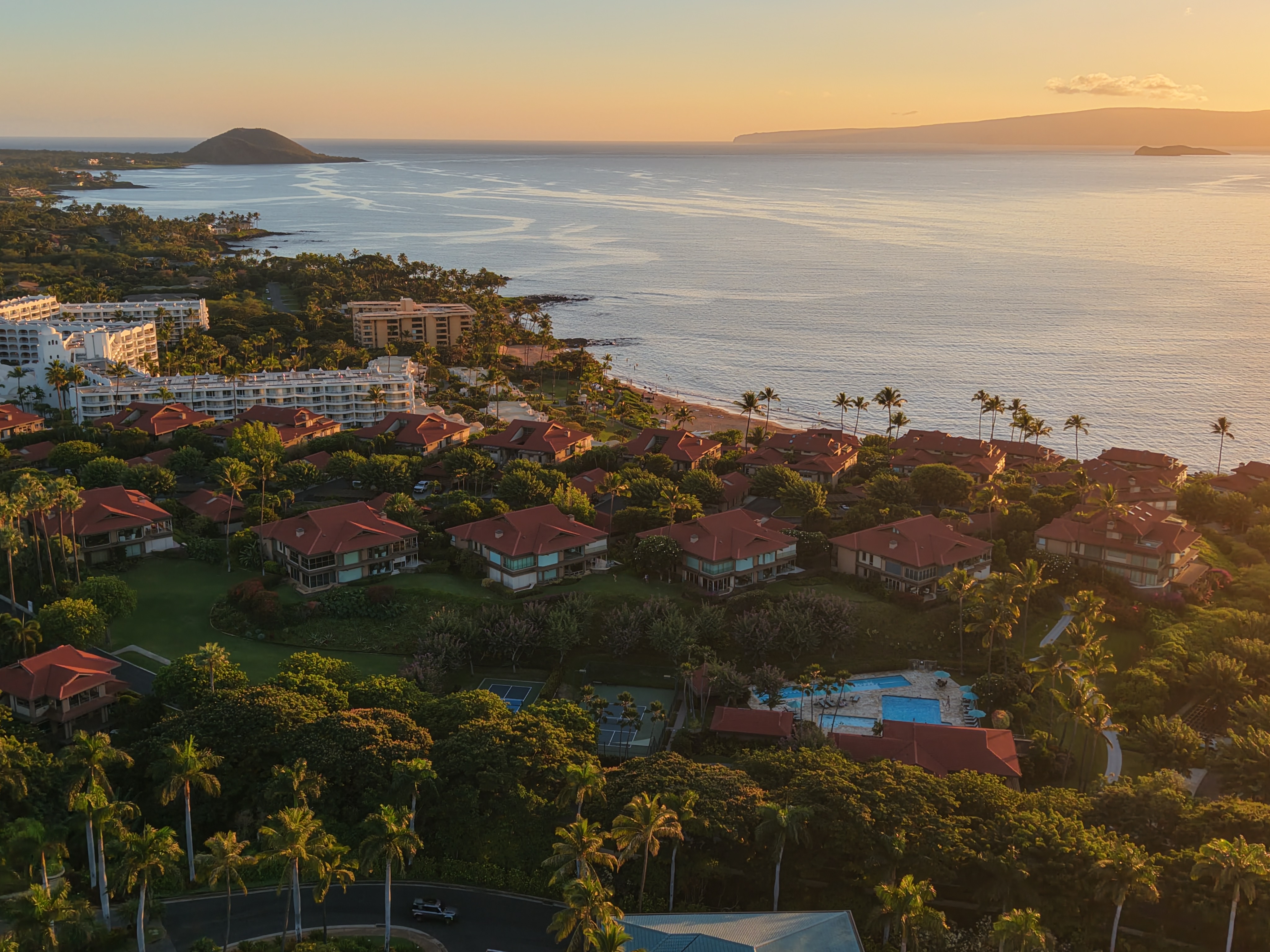 Golden hour aerial photograph of Wailea Point beachfront resort condominiums with red tile roofs, tropical landscaping, tennis courts, swimming pools, and Pacific Ocean views toward Molokini Crater