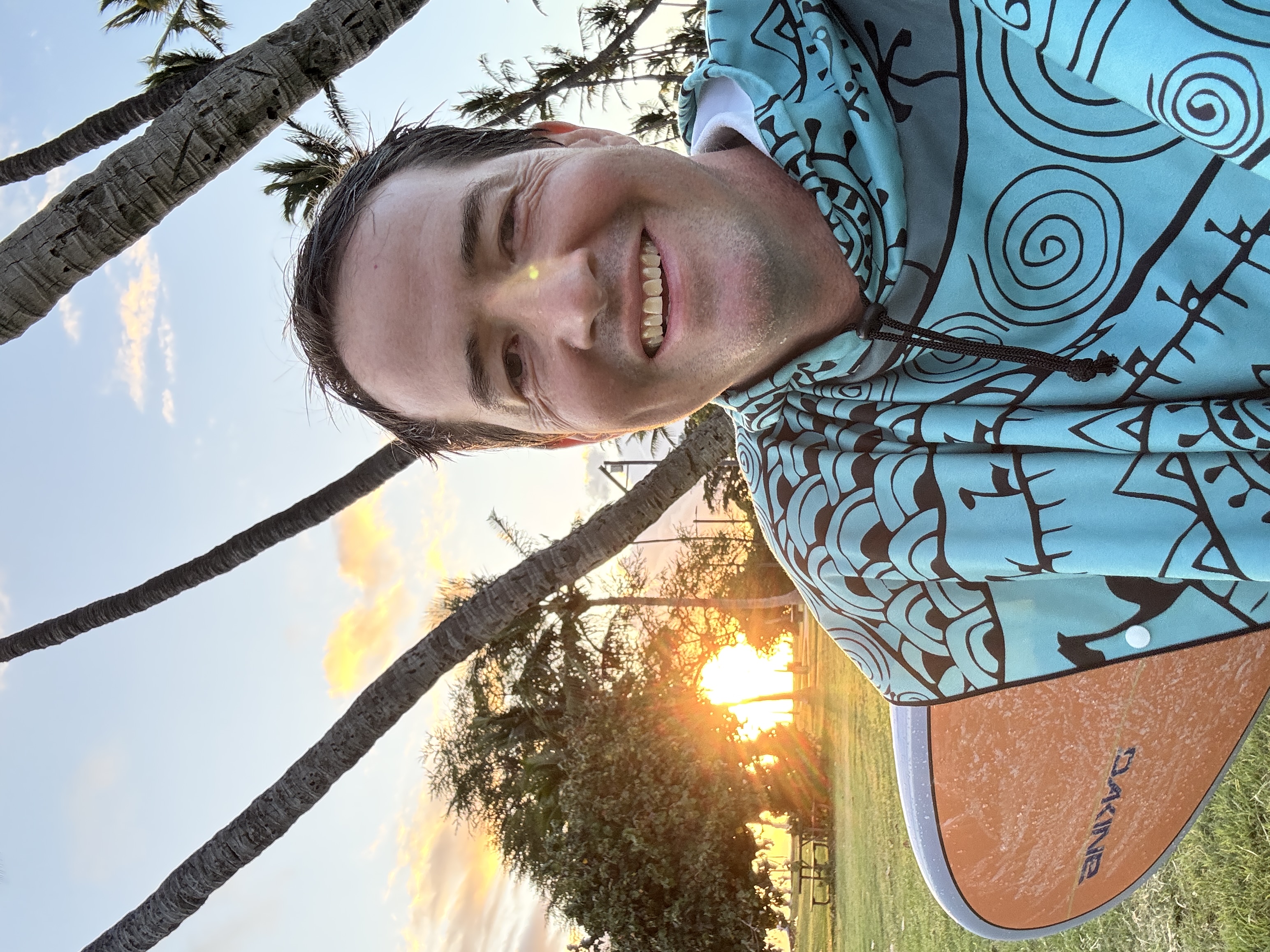 Benjamin Finnerty and his surfboard surfboard at sunset on a Maui beach, capturing the balance between island lifestyle and real estate career.