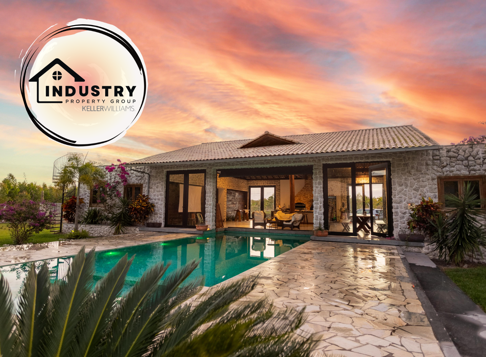 Luxury stone villa with a modern open-concept design, featuring a sleek infinity pool and lush tropical landscaping. The sunset sky casts warm hues over the property, enhancing its serene and exclusive atmosphere.