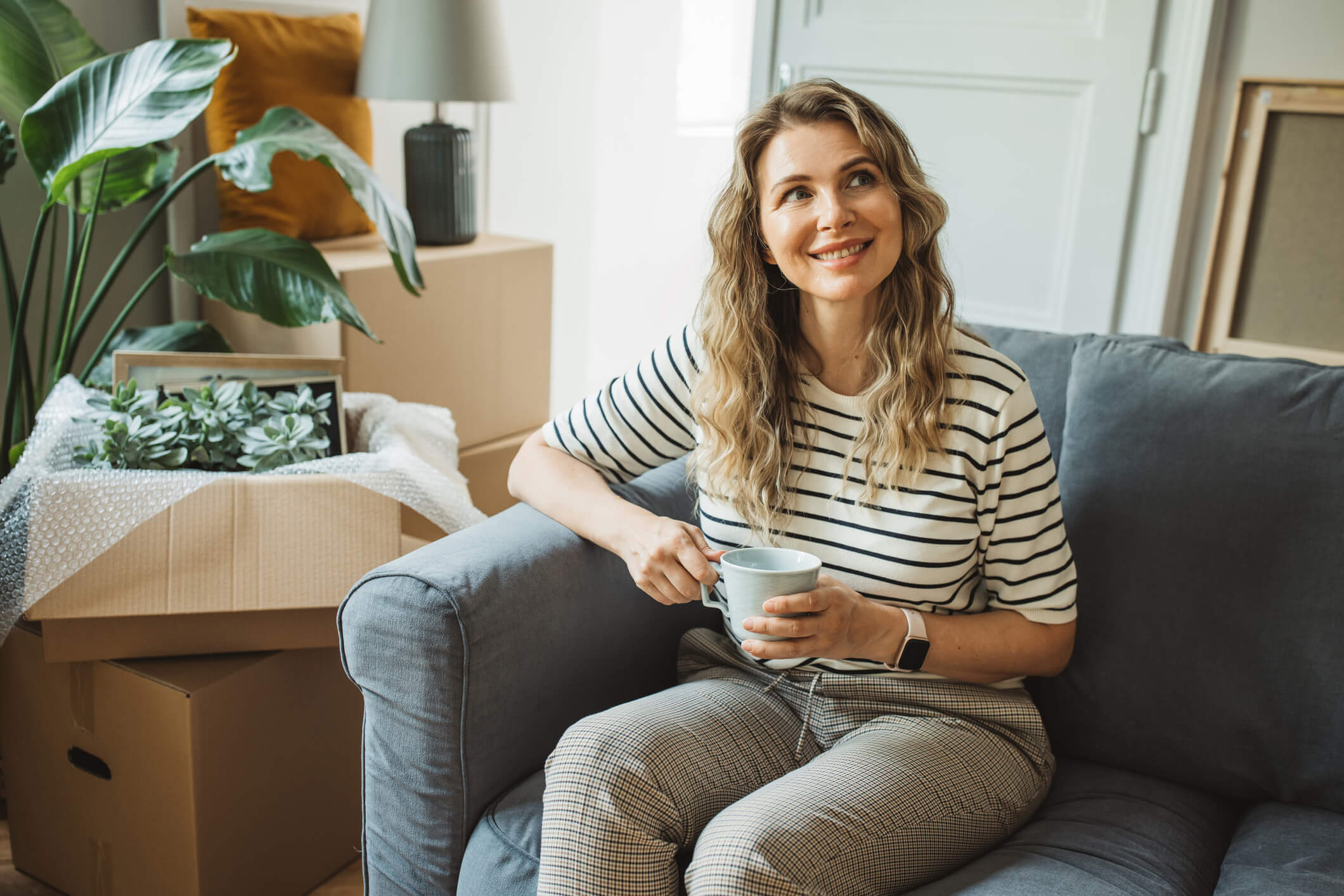 Woman smiling and drinking coffee in home filled with moving boxes