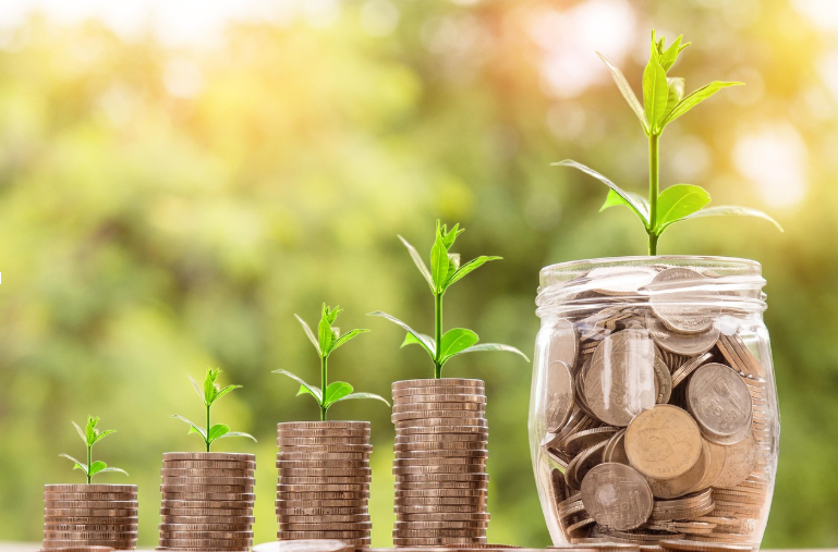 Growing stacks of coins and a jar of savings with sprouting plants, representing mortgage interest deduction benefits and financial growth for homeowners.