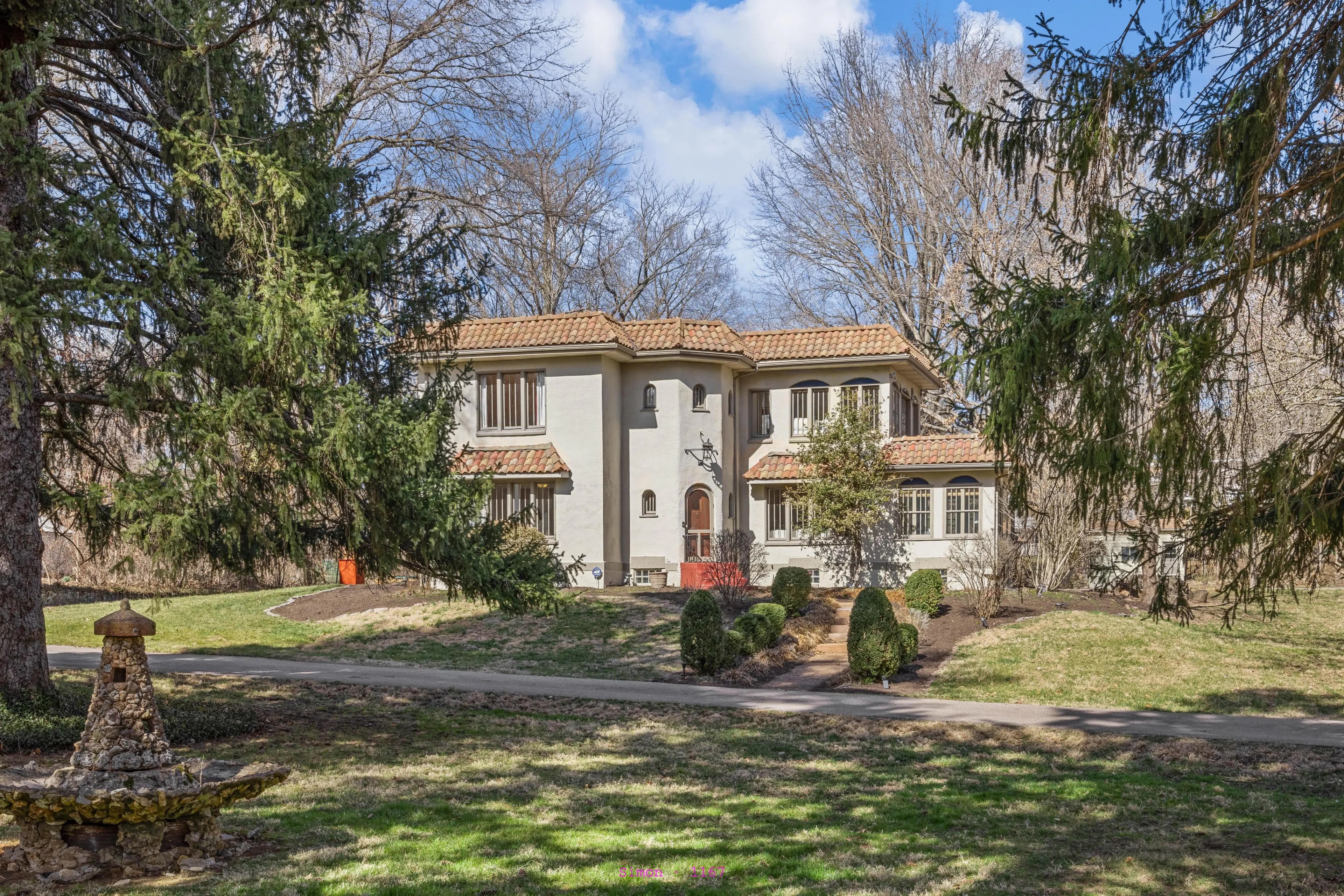 1926 Spanish revival estate in Webster Groves, Missouri, featuring terracotta tile roof, white stucco exterior, arched entry, and circular drive framed by mature evergreen trees on a nearly 1.5-acre lot.