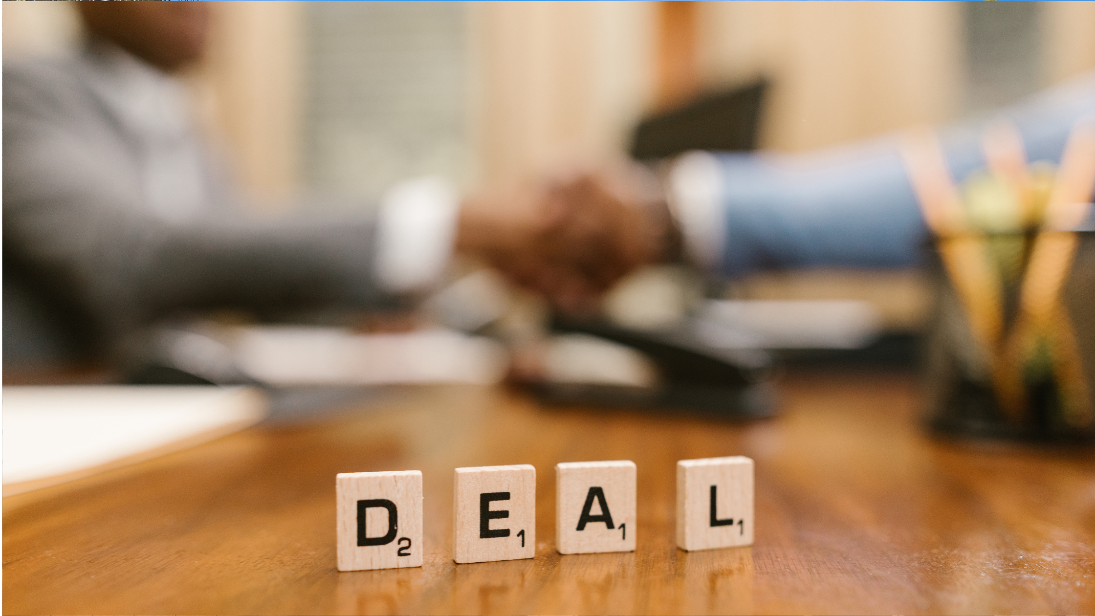Scrabble tiles spelling out DEAL on a table with 2 people shaking hands