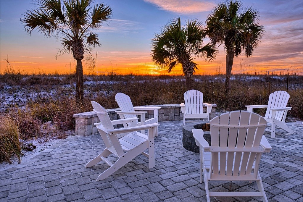Four adirondack chairs on a back patio around a firepit with a colorful sunset