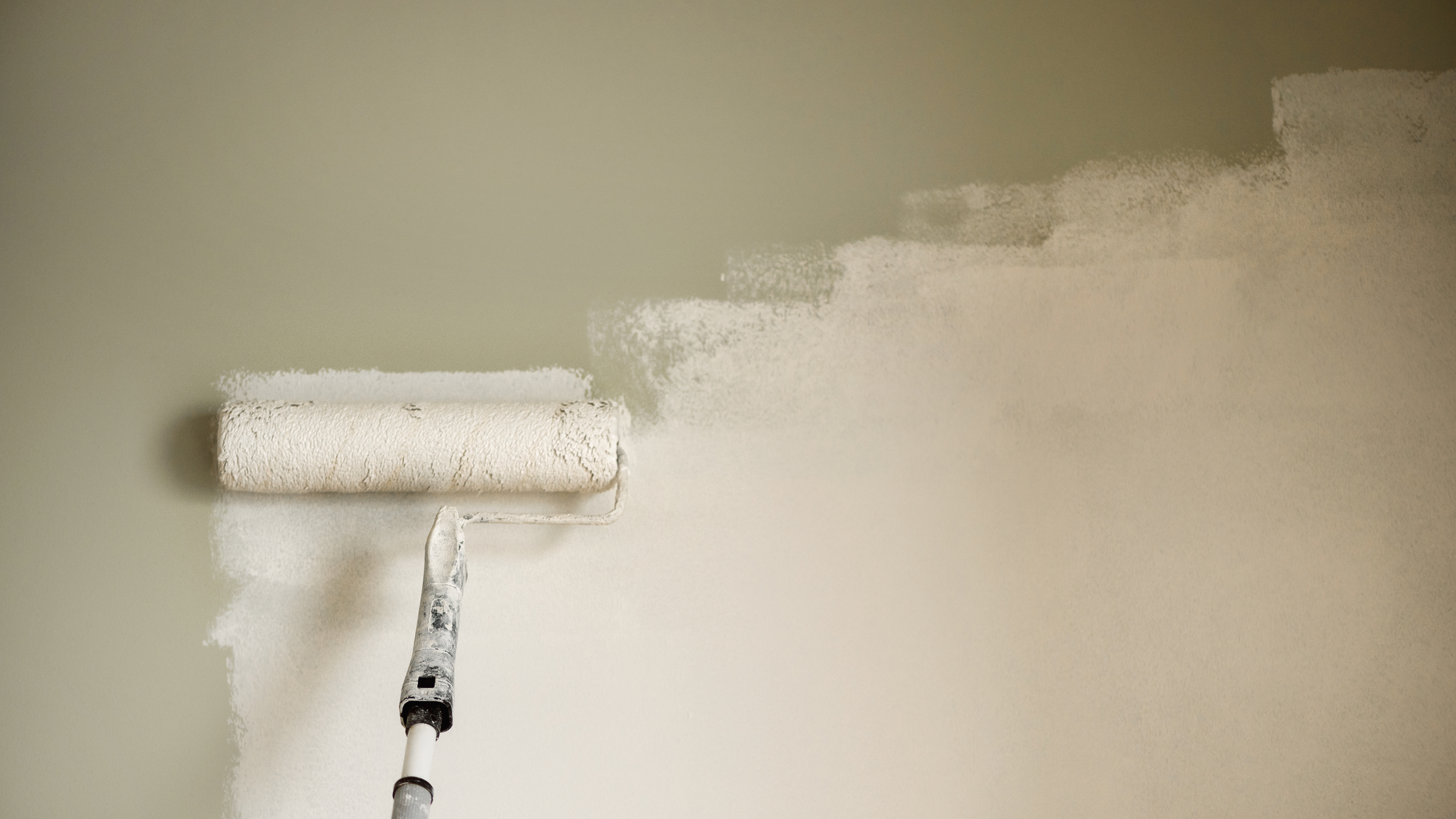 Paint roller applying white paint to wall