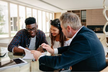 Real estate agent reviewing documents with a smiling couple at a table in a modern home.