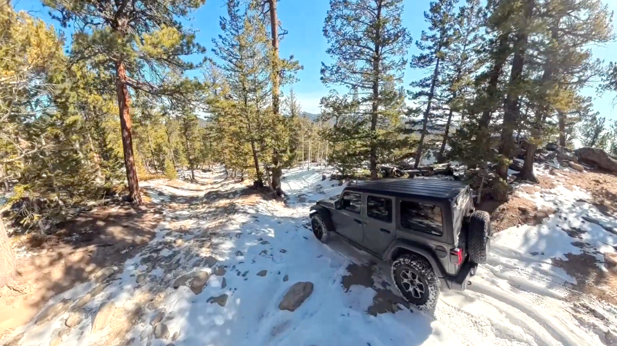 Jeep on snowy Bunce School Road in winter near Allenspark Colorado with pine trees